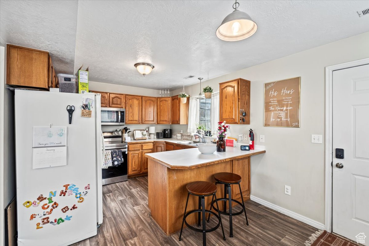 Kitchen featuring a breakfast bar, dark hardwood, appliances with stainless steel finishes, and kitchen peninsula