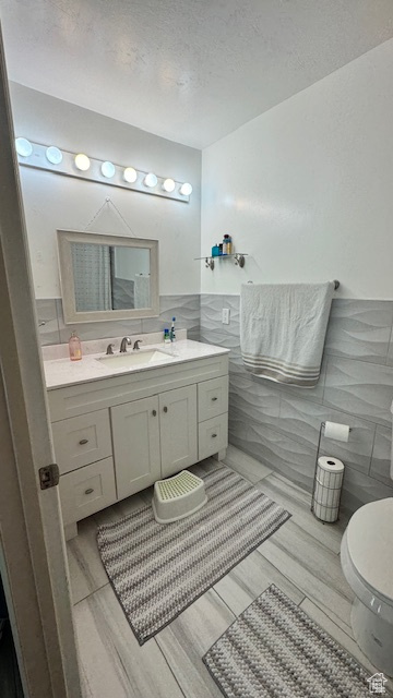 Bathroom with a textured ceiling, vanity, toilet, and tile walls