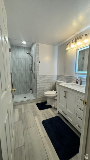 Bathroom featuring vanity, toilet, a tile shower, and tile walls