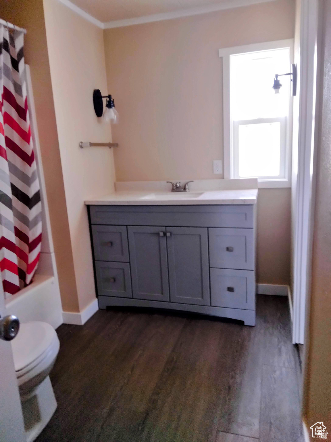 Full bathroom featuring hardwood / wood-style floors, vanity, toilet, shower / bath combo with shower curtain, and ornamental molding