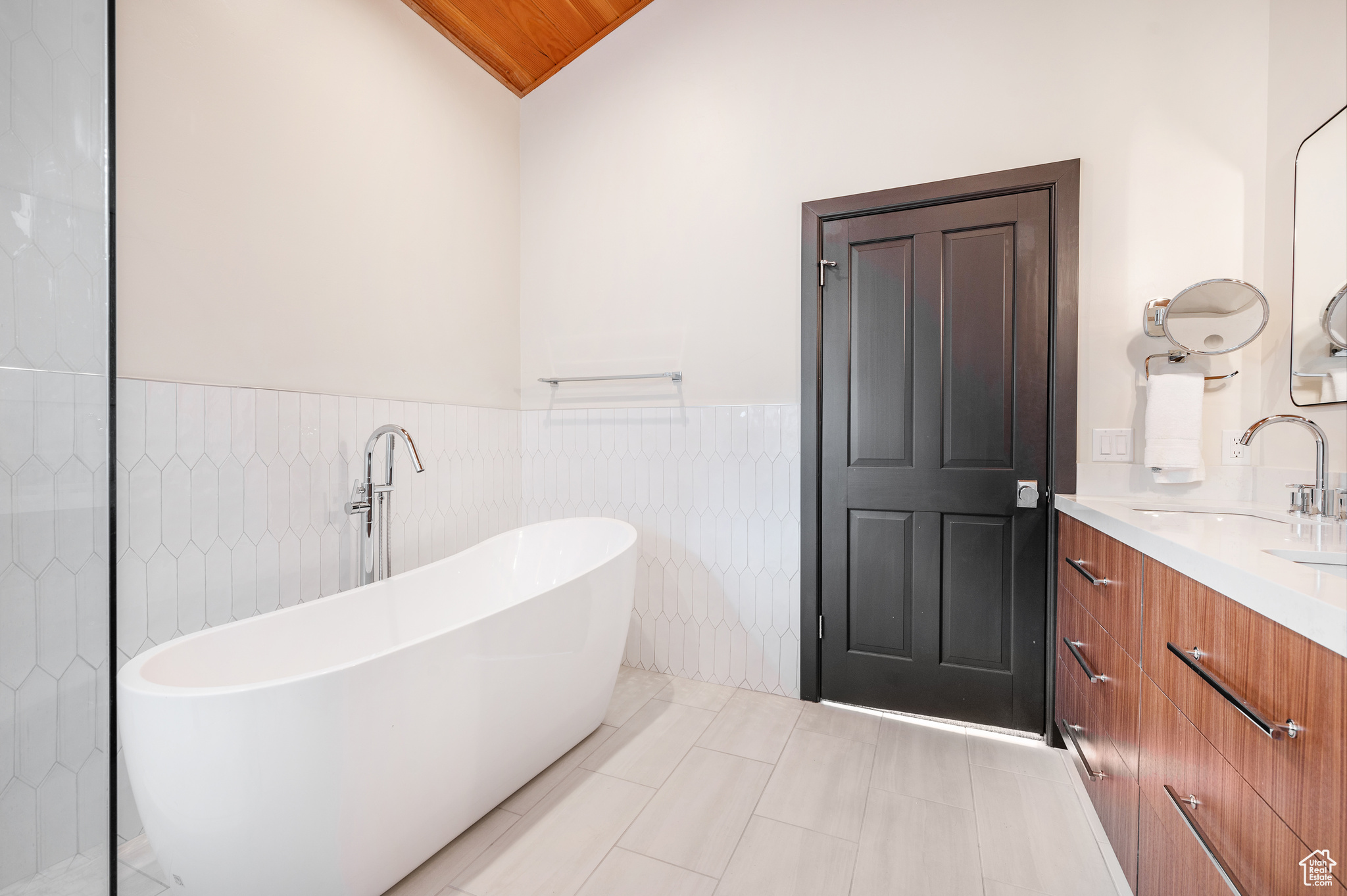 Bathroom featuring a bathtub, vanity, lofted ceiling, tile patterned flooring, and tile walls