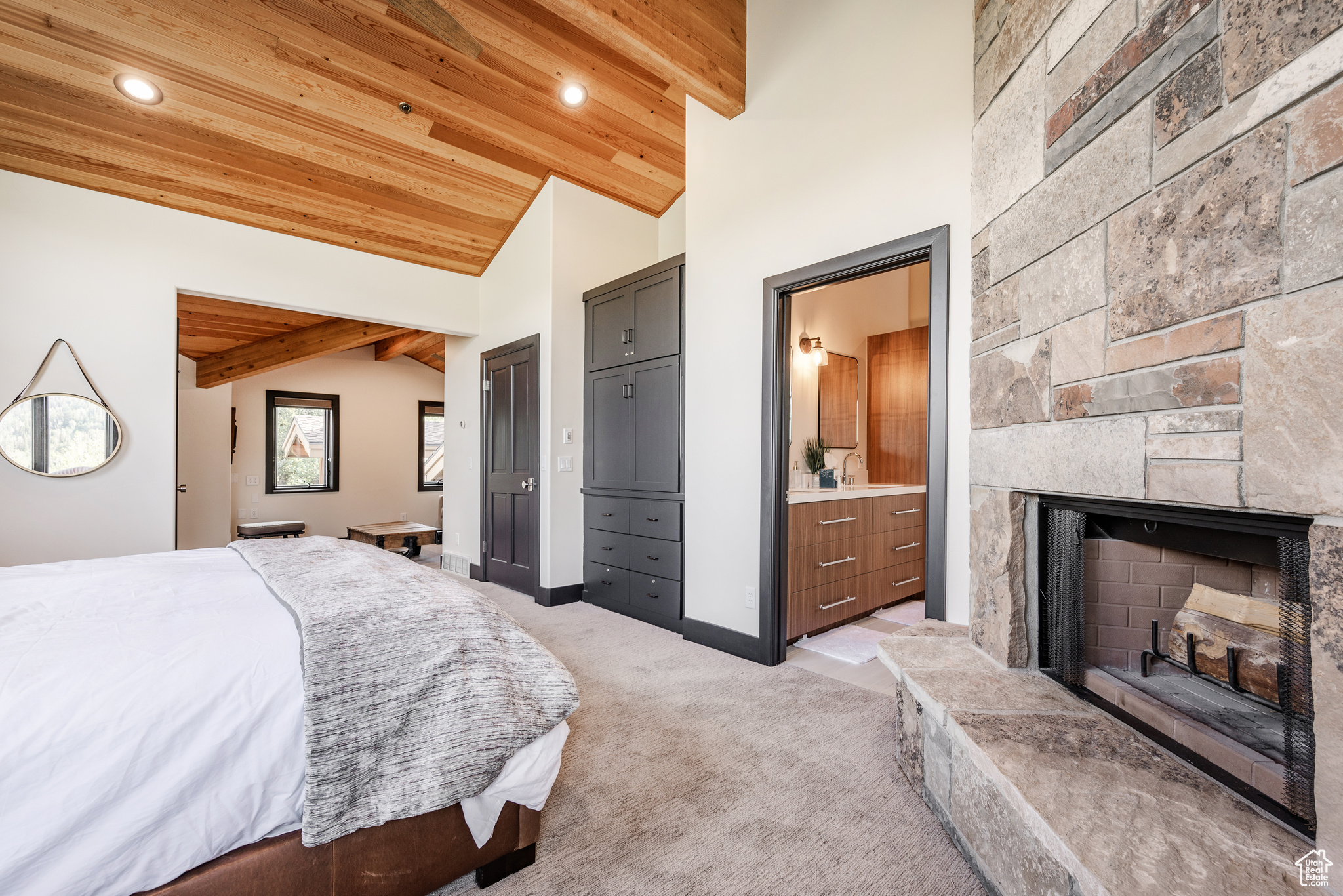 Carpeted bedroom featuring ensuite bathroom, vaulted ceiling, wooden ceiling, and a stone fireplace