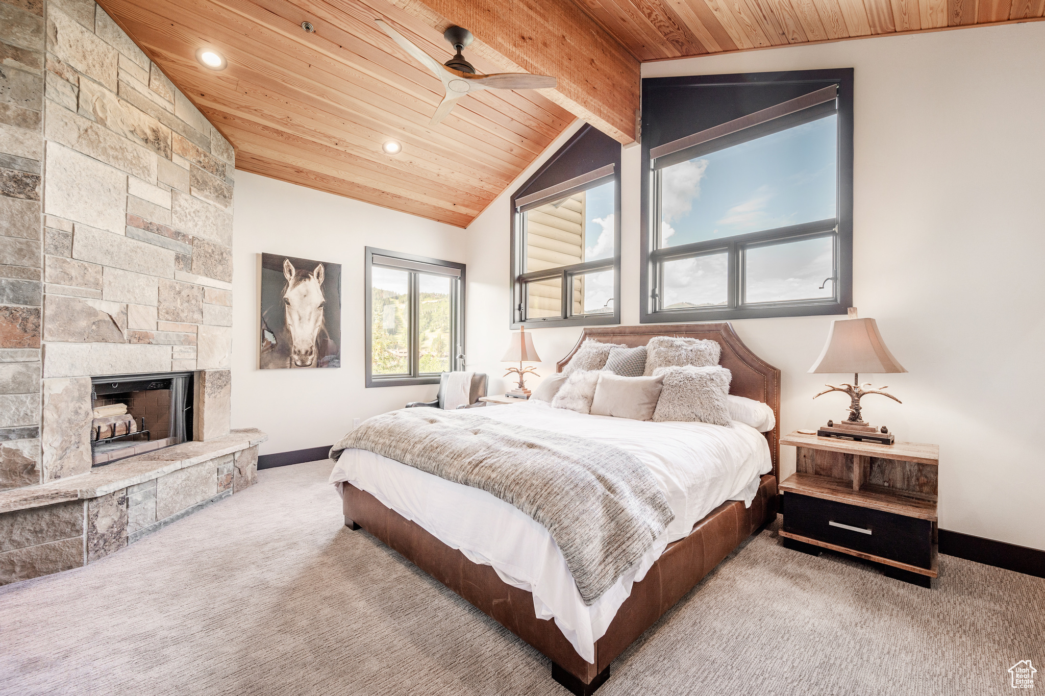 Carpeted bedroom featuring lofted ceiling with beams, ceiling fan, a stone fireplace, and wood ceiling