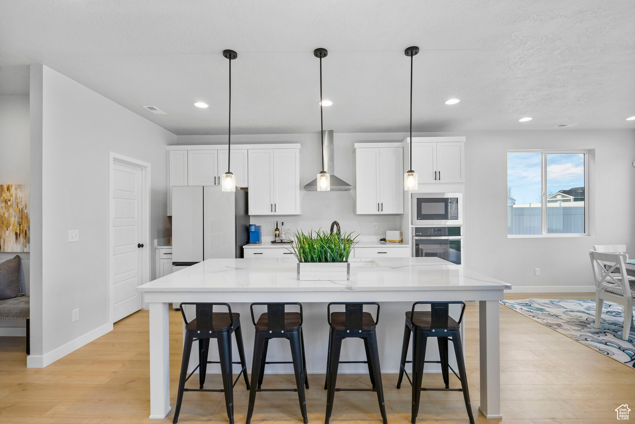 Kitchen with built in microwave, wall chimney range hood, white refrigerator, oven, and white cabinetry