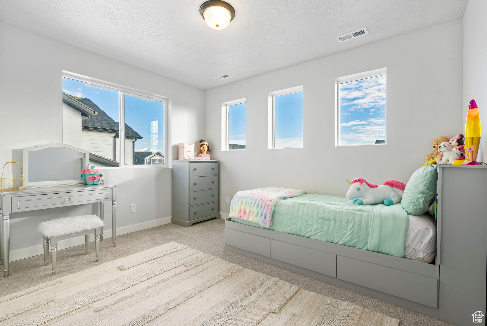 Bedroom with a textured ceiling, light carpet, and multiple windows