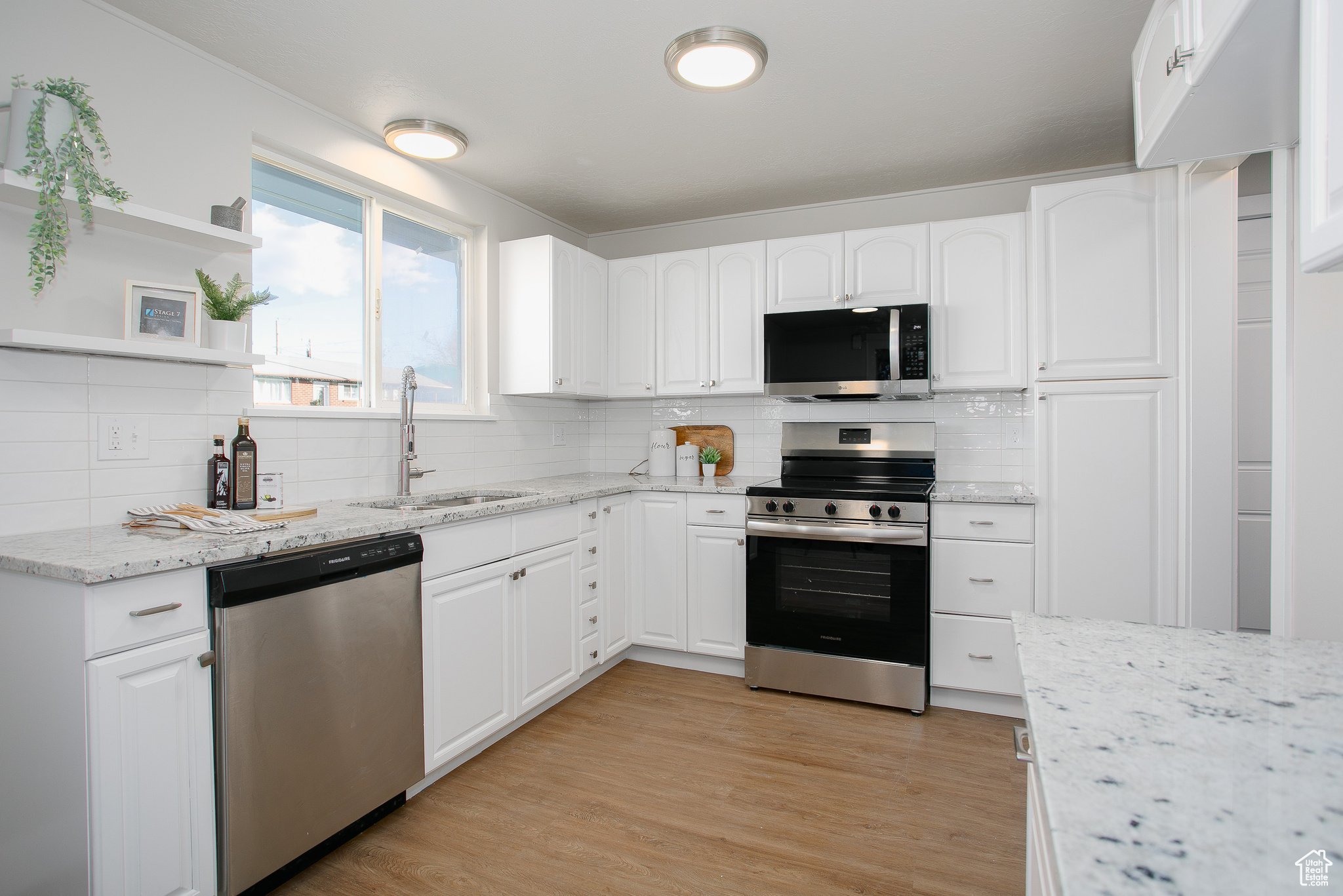 Kitchen featuring appliances with stainless steel finishes, tasteful backsplash, sink, light hardwood / wood-style flooring, and white cabinetry