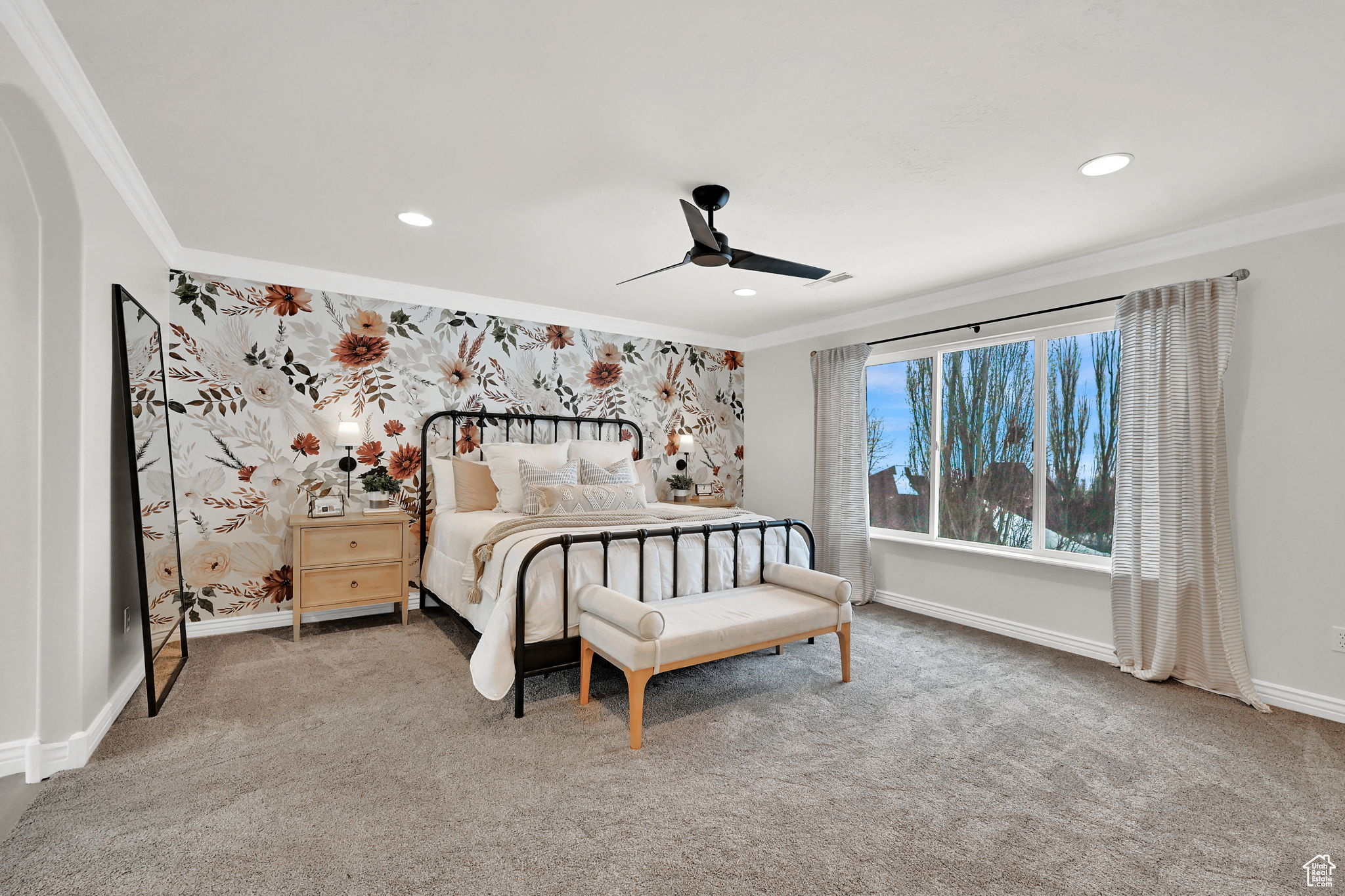 Carpeted bedroom featuring ceiling fan, crown molding, and wall papered feature wall