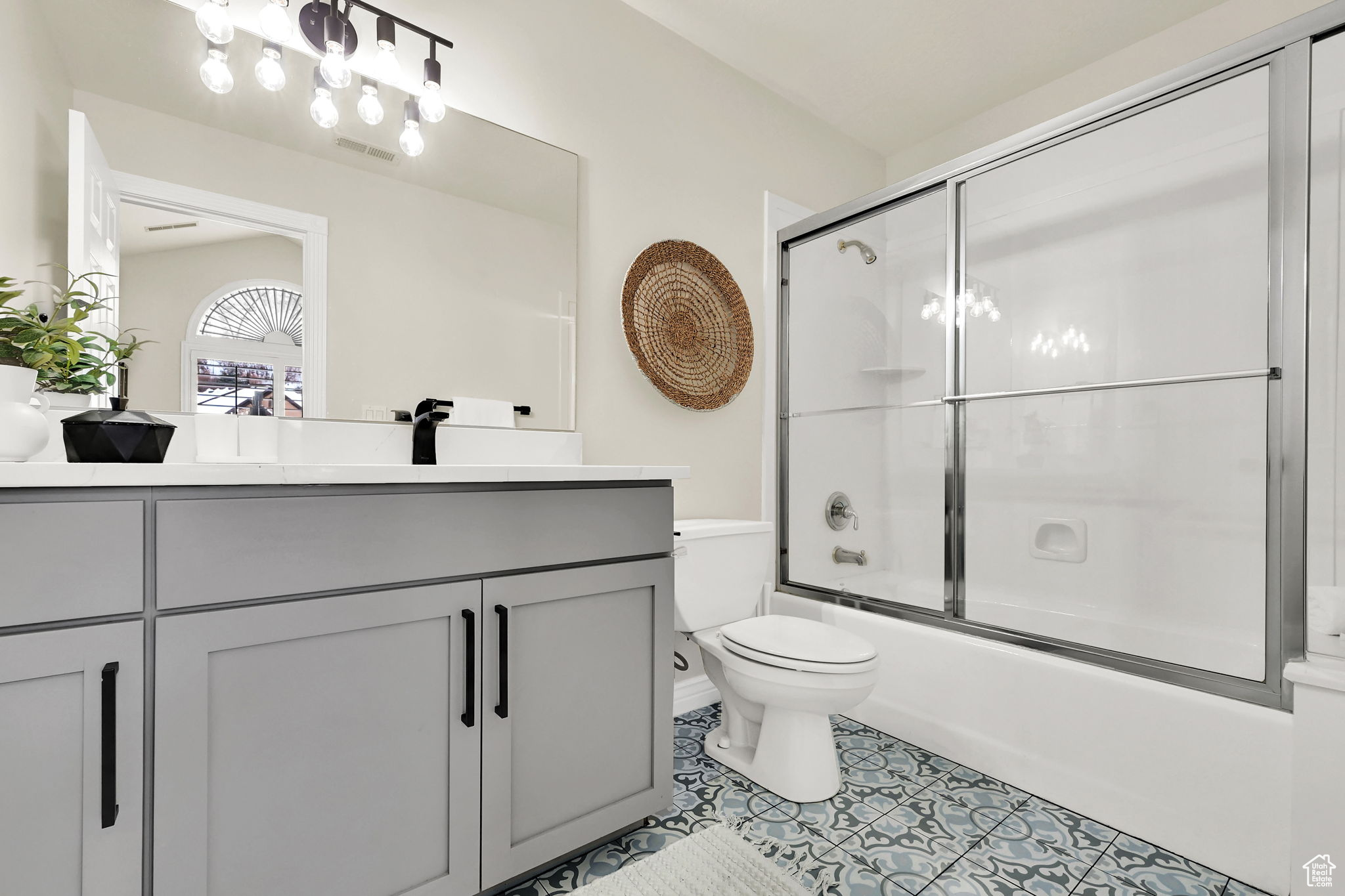 Full bathroom with tile patterned floors, vanity, enclosed tub / shower combo, and toilet