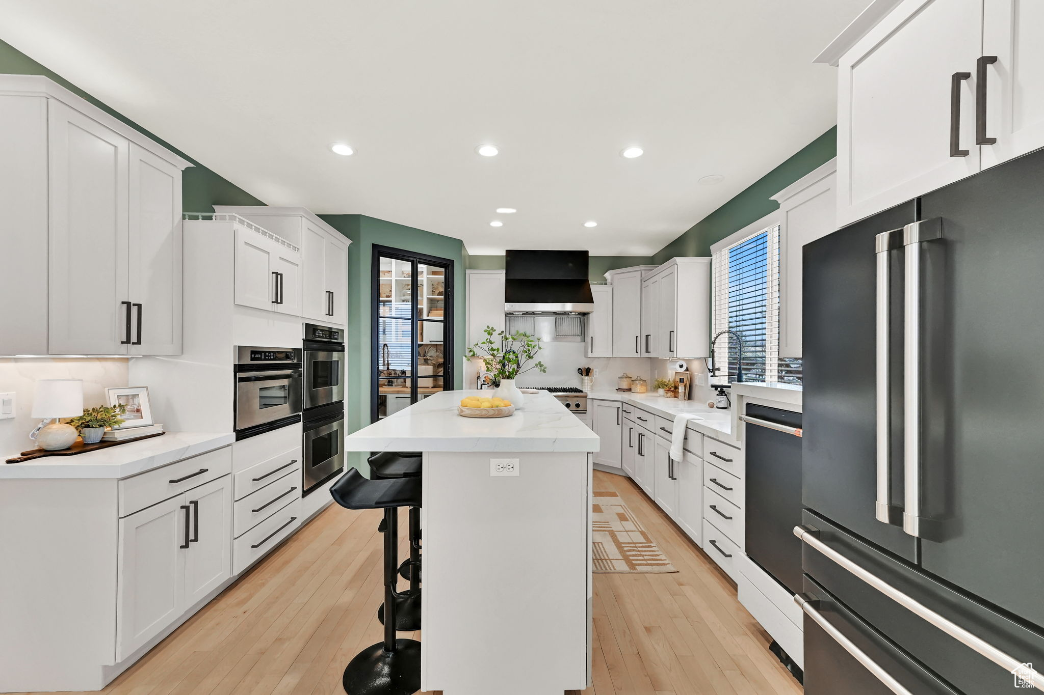 Kitchen with appliances with stainless steel finishes, wall exhaust hood, light grey cabinets, a center island, and a breakfast bar area