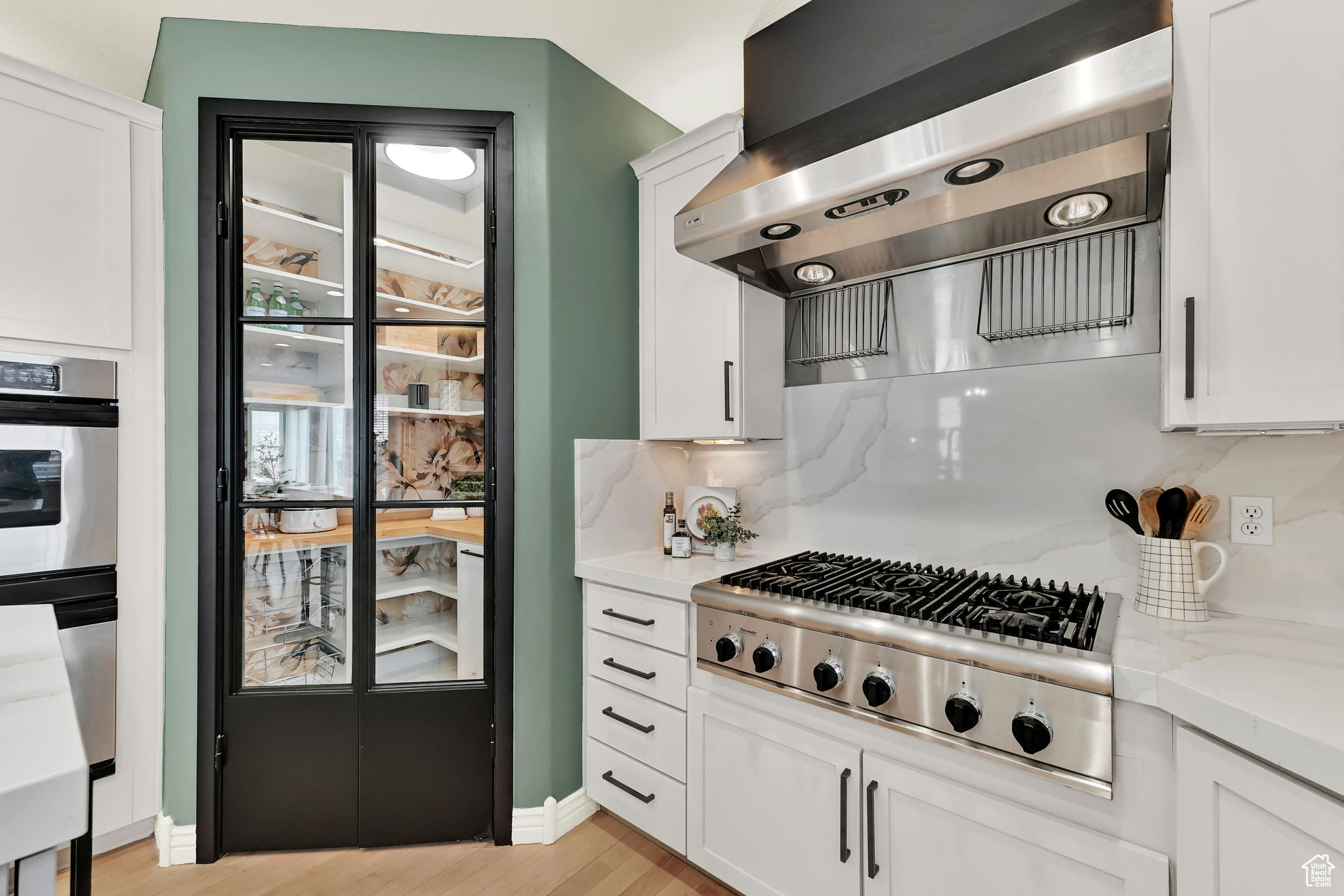 Kitchen featuring light grey cabinetry, quartz backsplash, exhaust hood, and appliances with stainless steel finishes