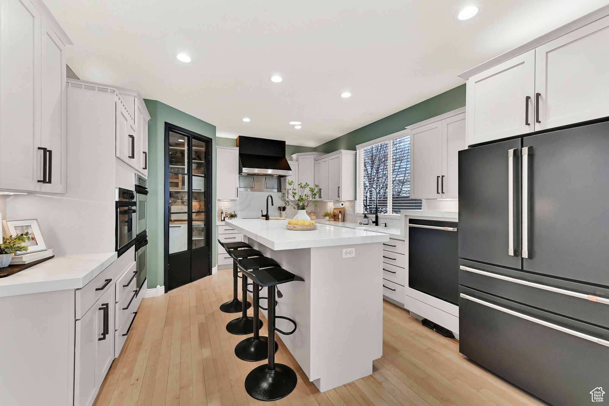 Kitchen featuring dishwasher, light grey cabinets, wall exhaust hood, high end fridge, and a breakfast bar area