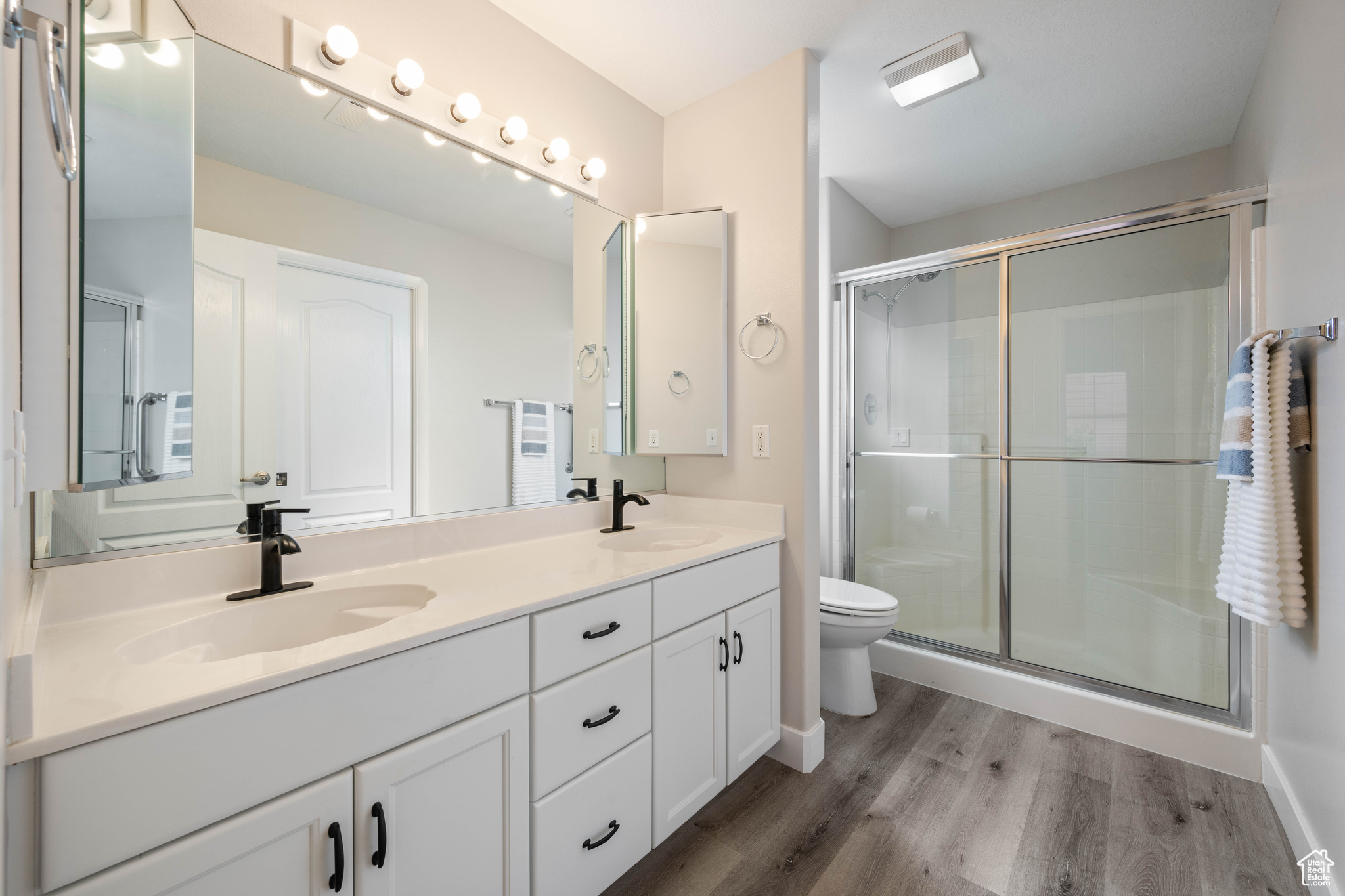Bathroom featuring wood finished floors, a stall shower, toilet, and double sinks