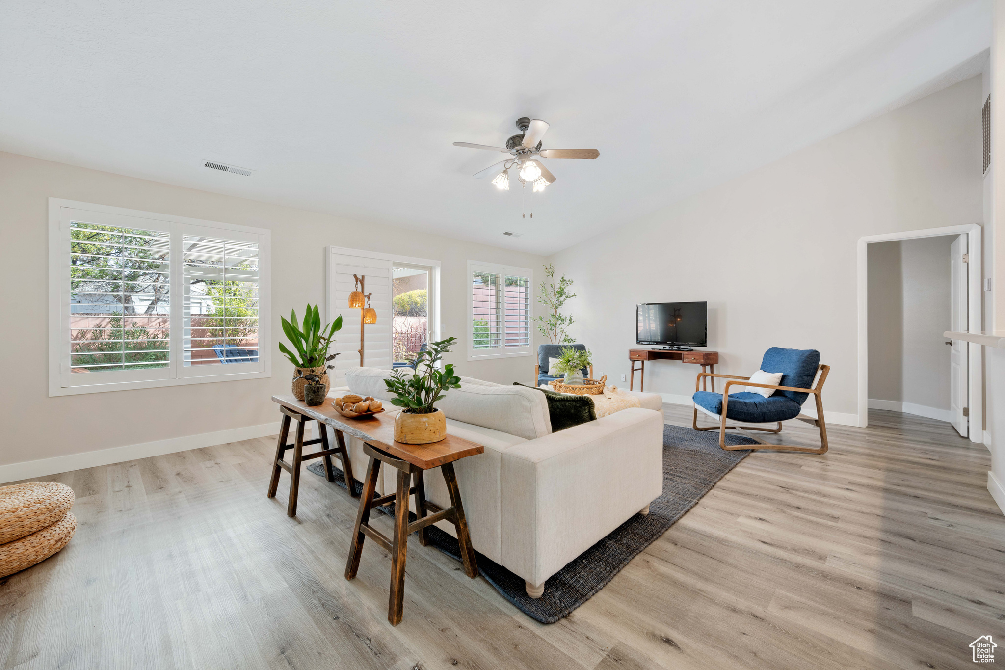 Living area featuring visible vents, baseboards, lofted ceiling, light wood-style flooring, and a ceiling fan