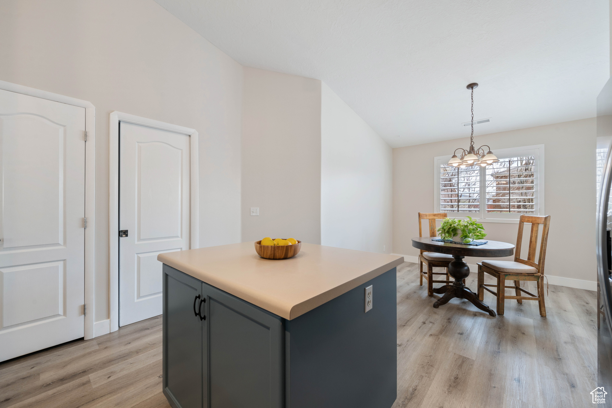 Kitchen featuring pendant lighting, light wood-style flooring, a center island, an inviting chandelier, and vaulted ceiling