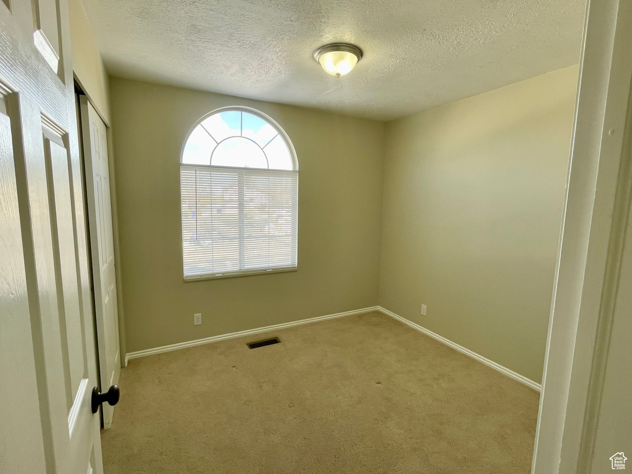 Empty room with light carpet and a textured ceiling