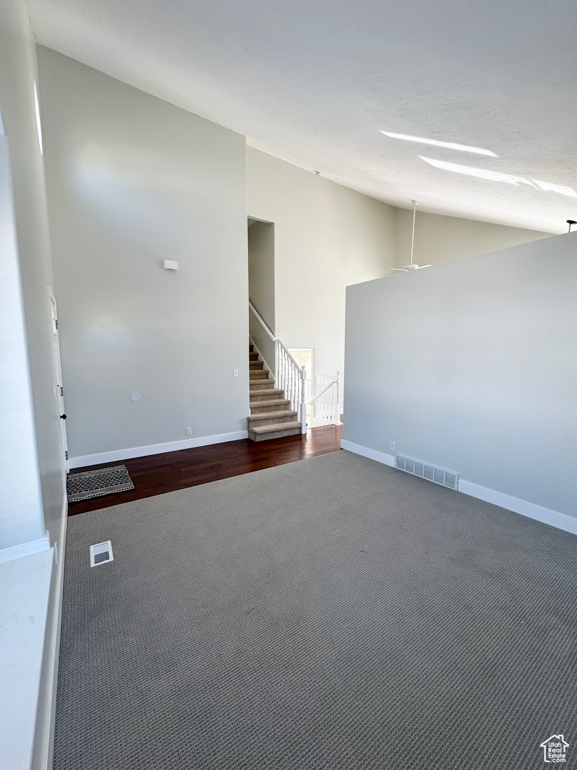 Carpeted empty room featuring visible vents, vaulted ceiling, stairway, and baseboards
