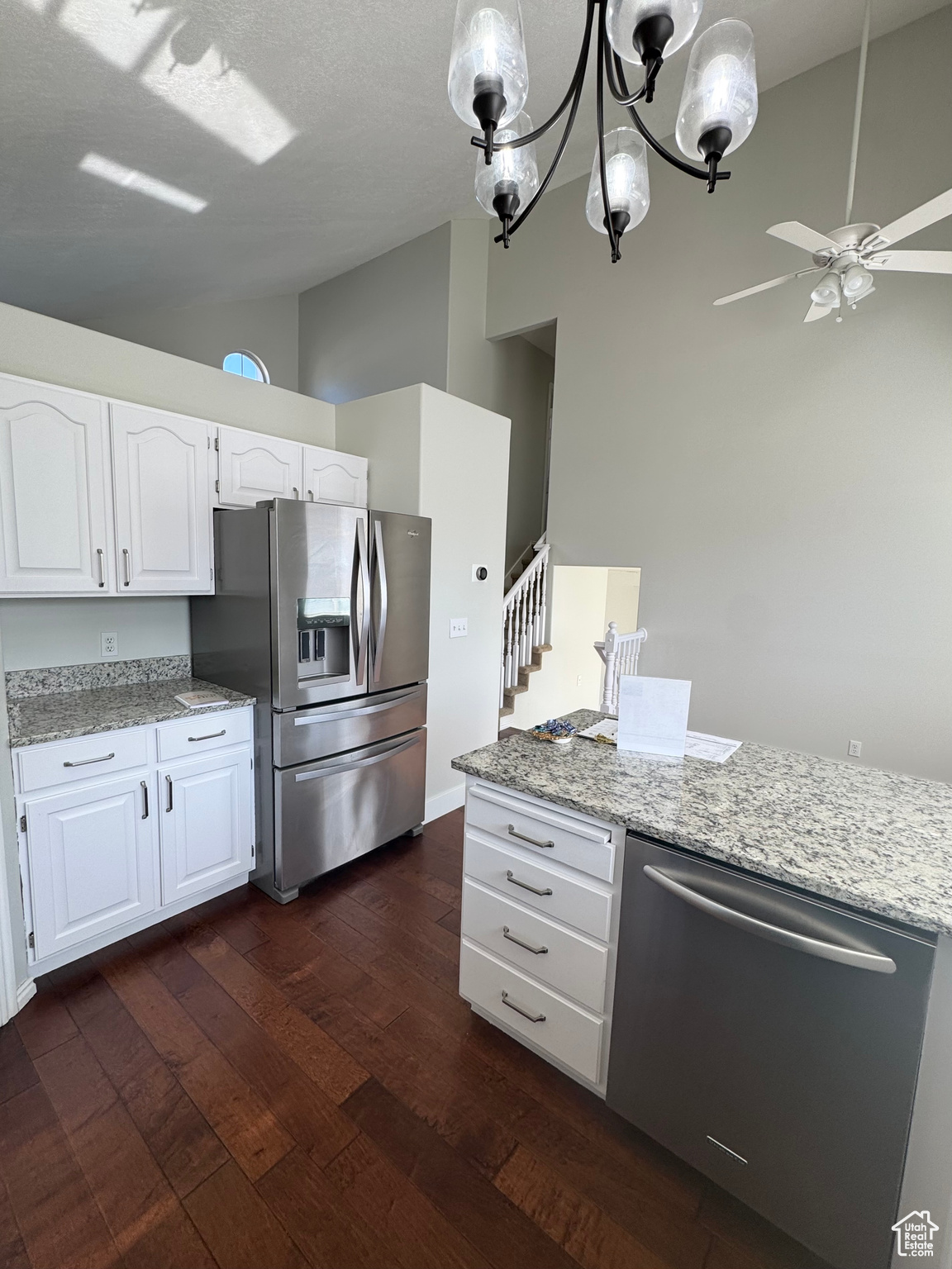 Kitchen with lofted ceiling, stainless steel appliances, white cabinets, light stone countertops, and dark wood finished floors