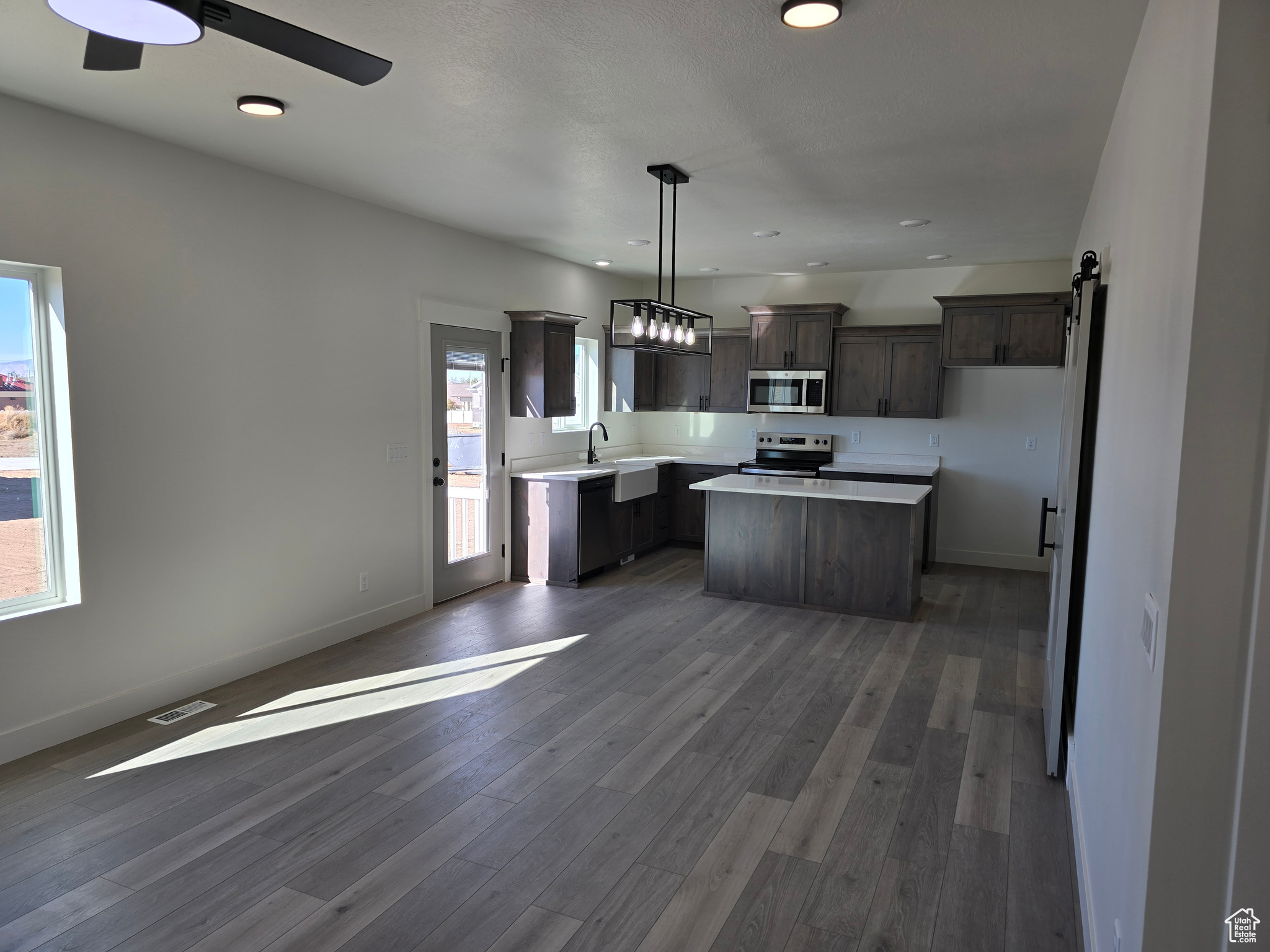 Kitchen featuring dark hardwood / wood-style flooring, stainless steel appliances, a barn door, decorative light fixtures, and a center island