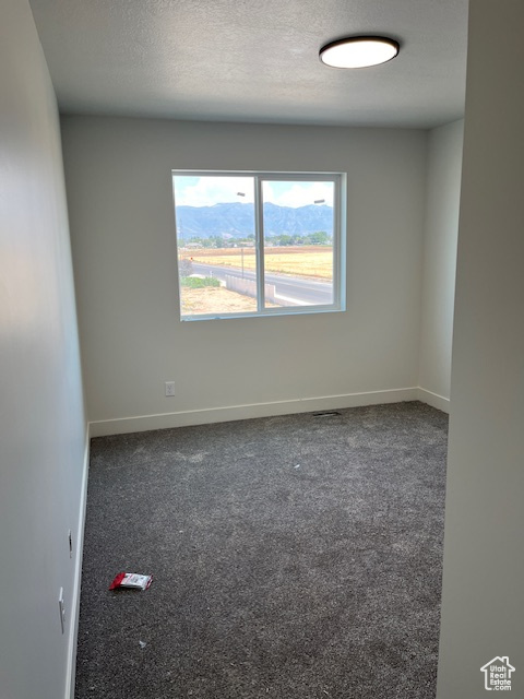 Empty room featuring dark carpet and a textured ceiling