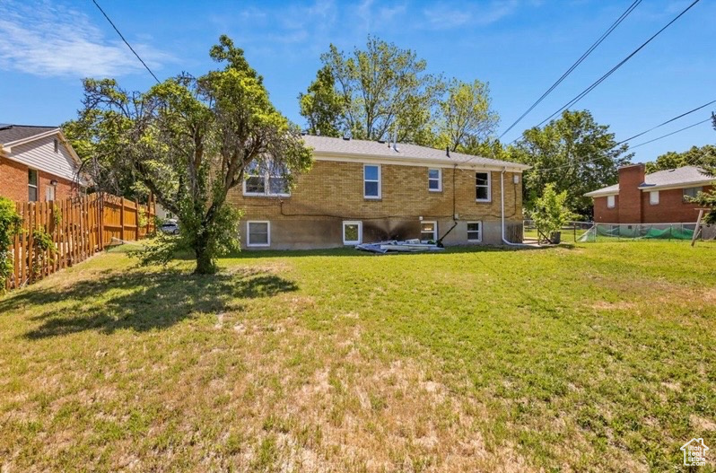 Back of property with brick siding, fence, and a yard