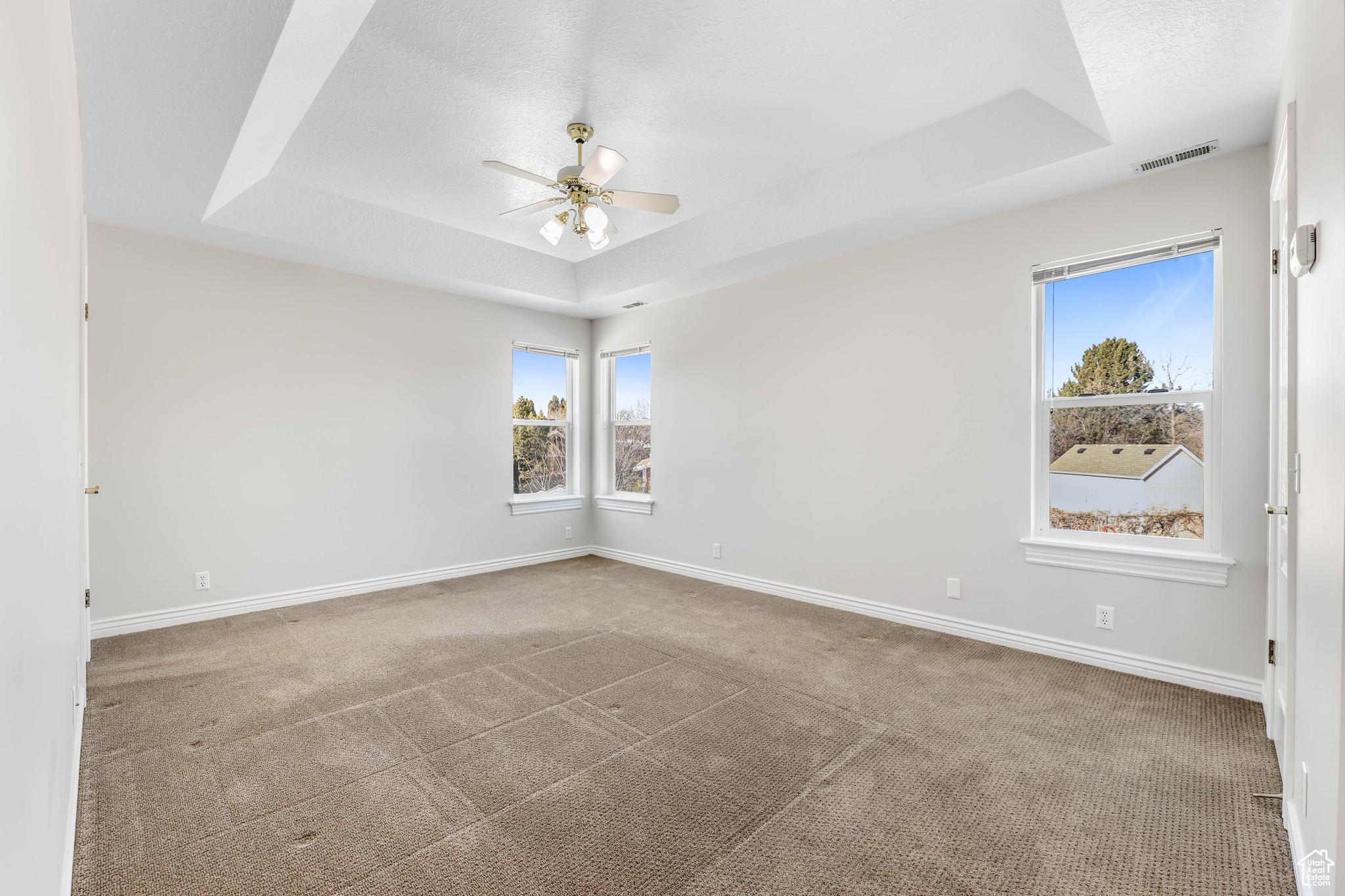 Carpeted spare room featuring ceiling fan, a raised ceiling, and a textured ceiling