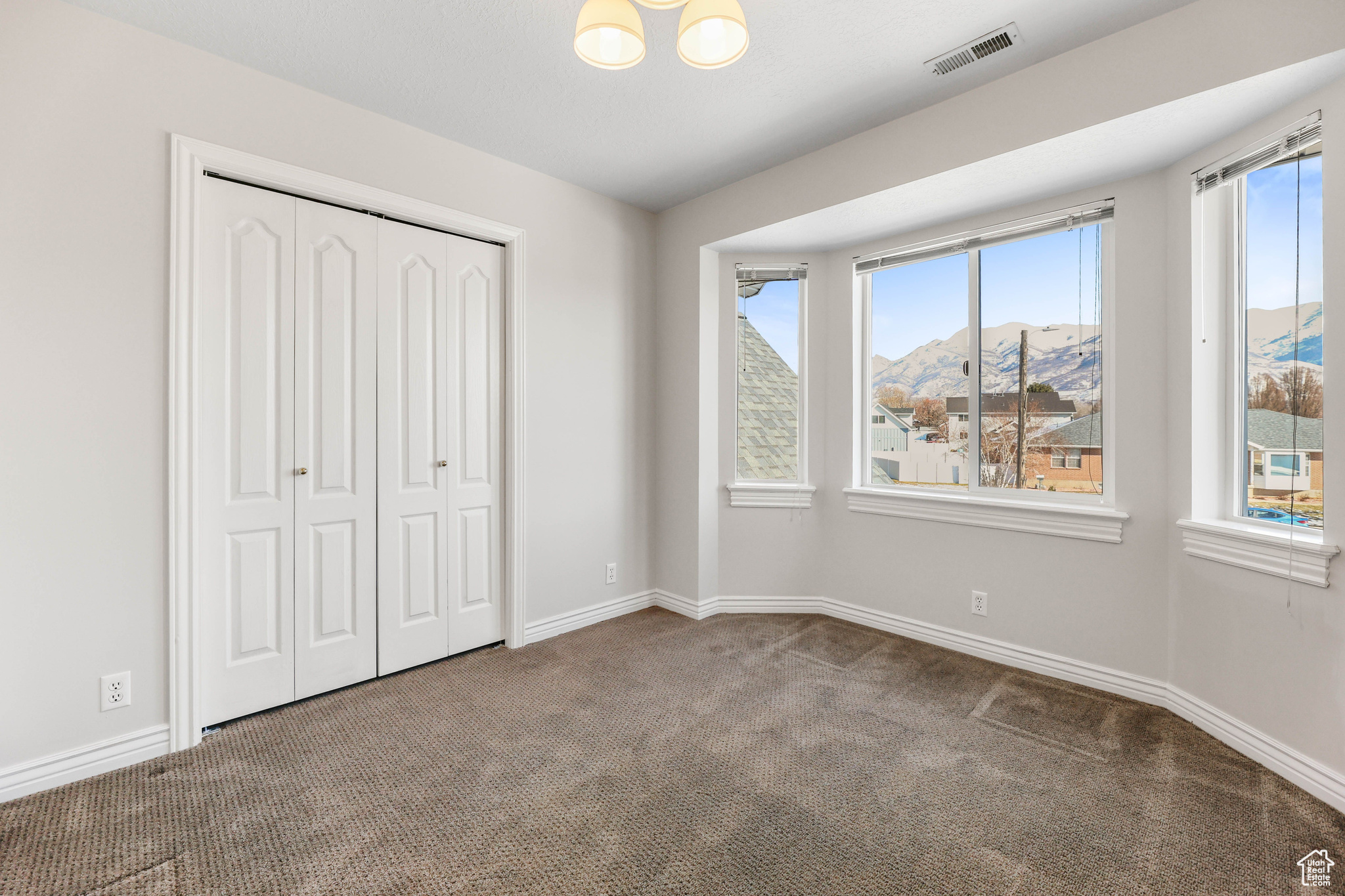 Unfurnished bedroom with carpet, a mountain view, a closet, and multiple windows