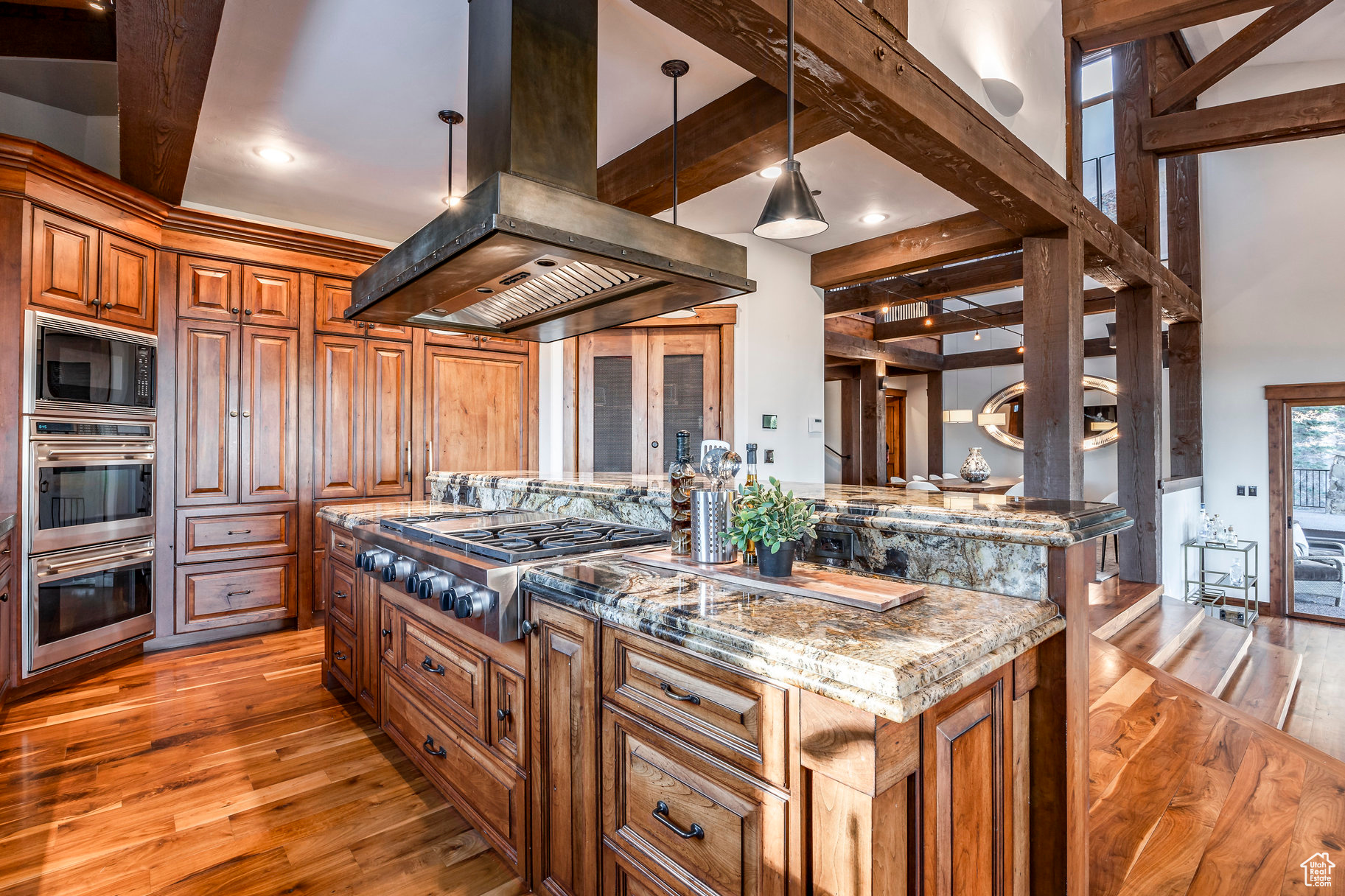 Kitchen with a center island, stainless steel appliances, light stone counters, pendant lighting, and island range hood