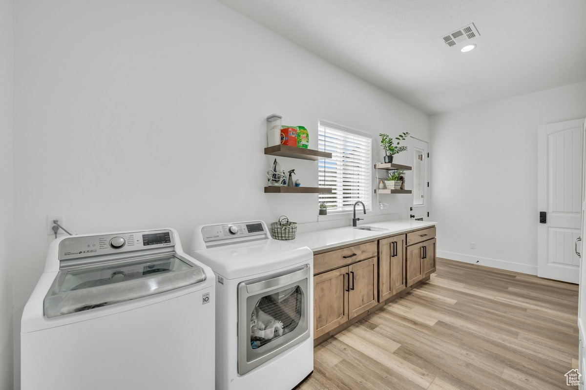Laundry area with separate washer and dryer, sink, cabinets, and light wood-type flooring