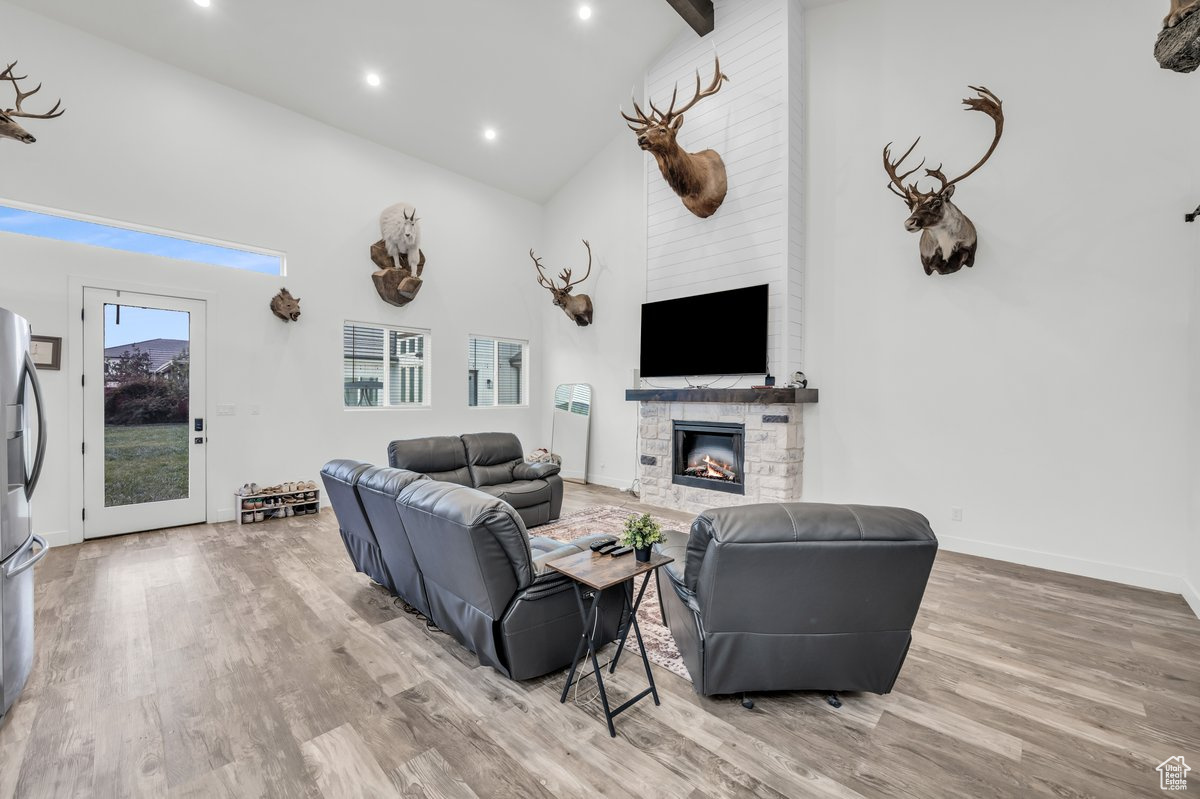 Living room with beamed ceiling, hardwood / wood-style floors, high vaulted ceiling, and a stone fireplace
