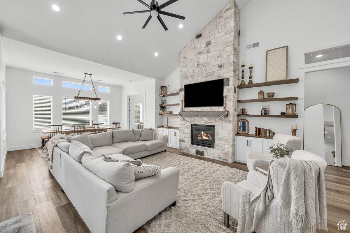 Living room with ceiling fan, wood-type flooring, a fireplace, and high vaulted ceiling
