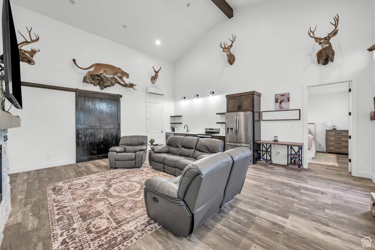 Living room with beamed ceiling, a wall mounted air conditioner, light hardwood / wood-style floors, and high vaulted ceiling