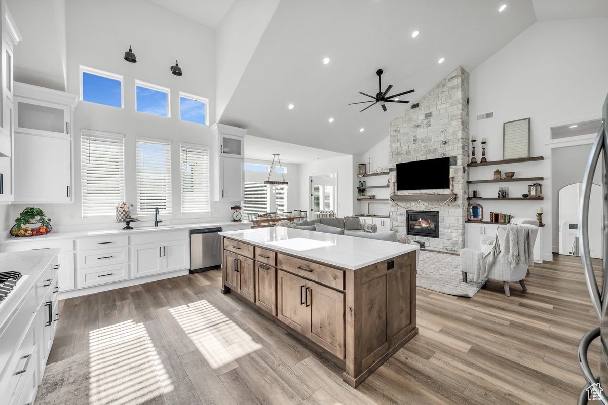 Kitchen featuring a stone fireplace, white cabinets, high vaulted ceiling, a kitchen island, and appliances with stainless steel finishes