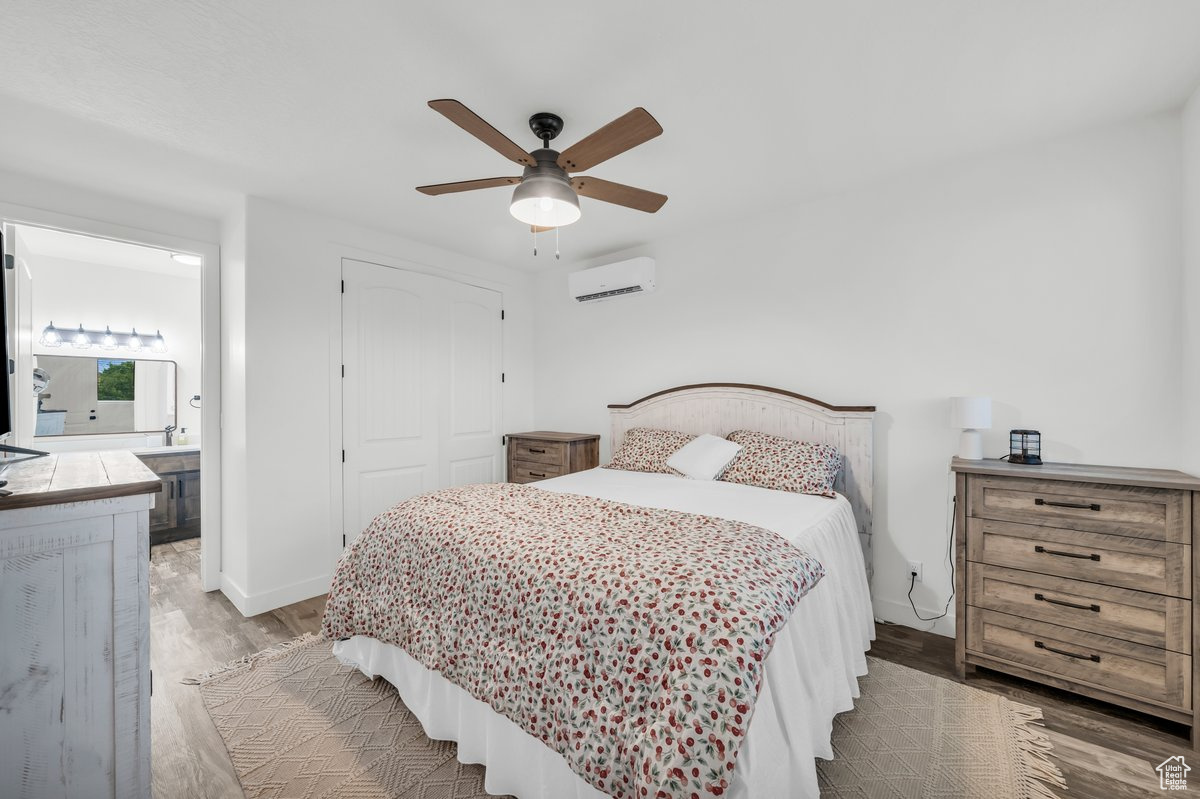 Bedroom with a wall unit AC, ceiling fan, hardwood / wood-style flooring, connected bathroom, and a closet