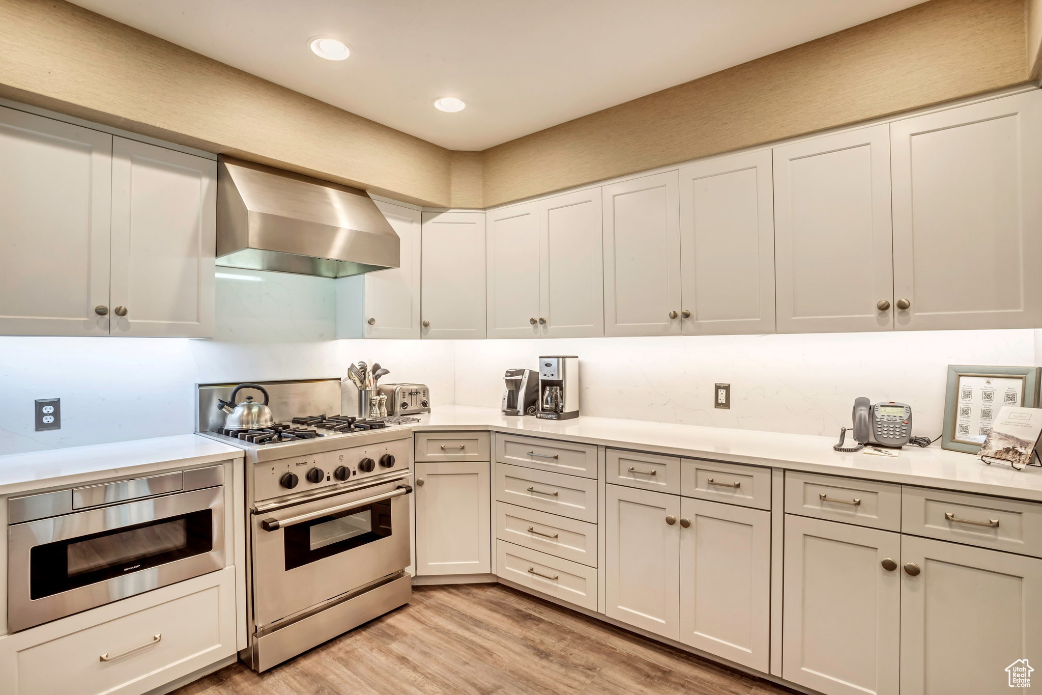 Kitchen featuring high end stove, light hardwood / wood-style floors, white cabinetry, and wall chimney range hood