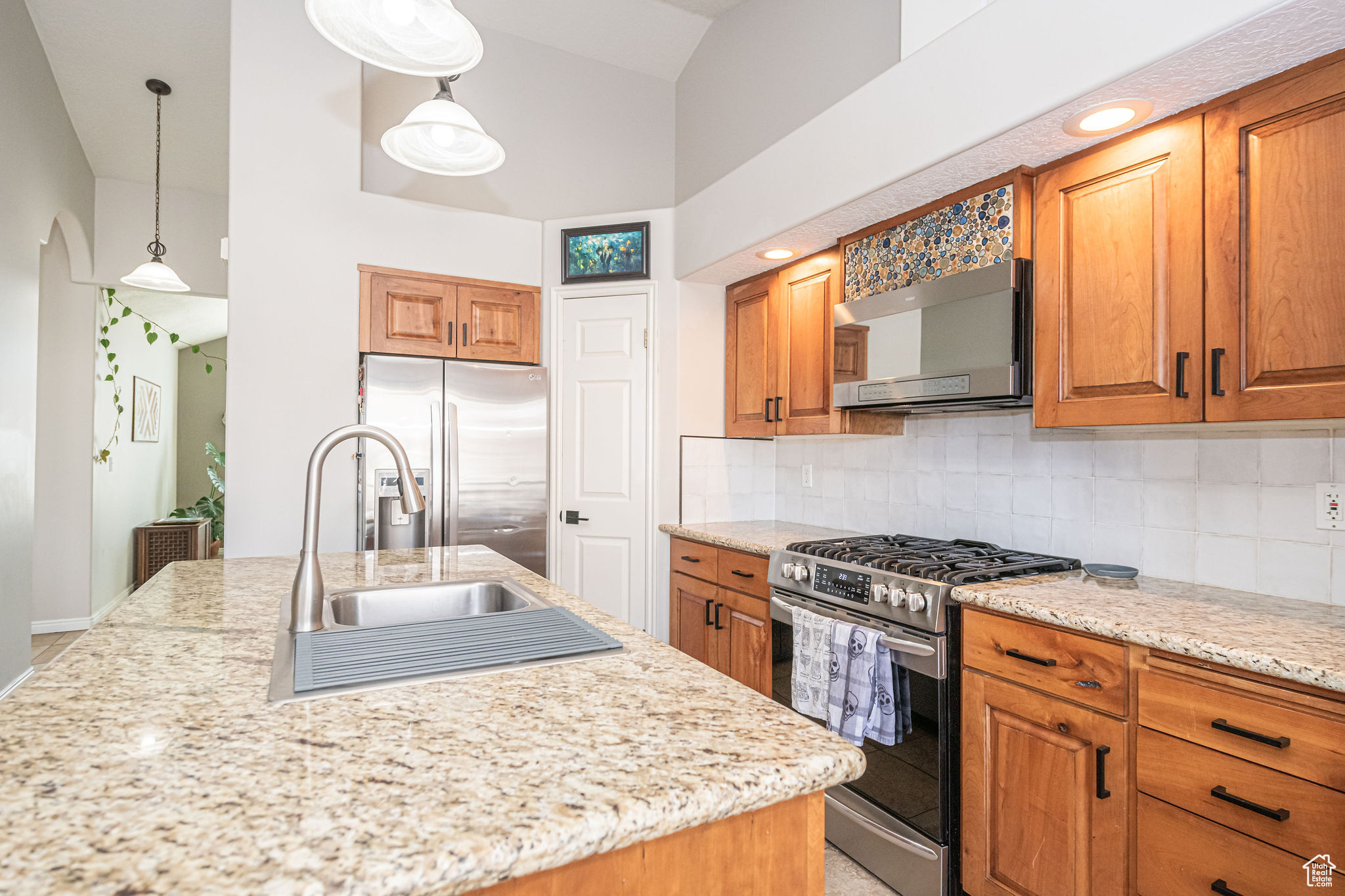 Kitchen featuring decorative backsplash, light stone countertops, a towering ceiling, appliances with stainless steel finishes, and decorative light fixtures
