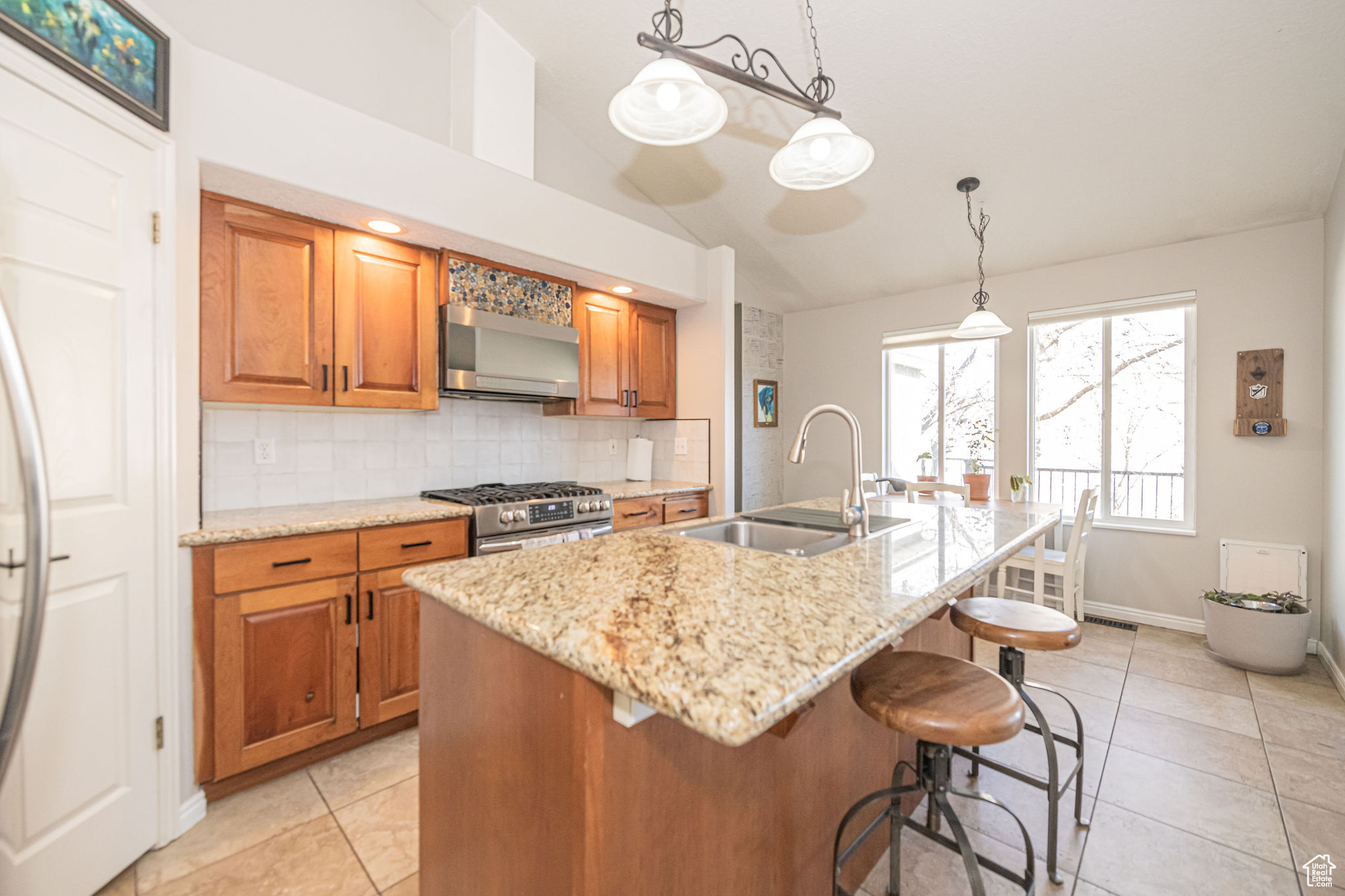 Kitchen with appliances with stainless steel finishes, vaulted ceiling, sink, a center island with sink, and hanging light fixtures
