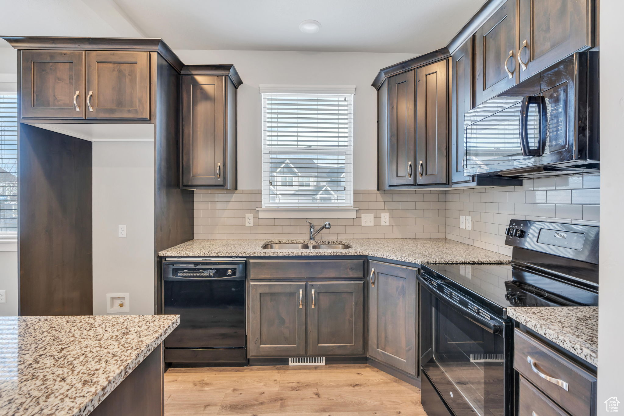 Kitchen with black appliances, light stone countertops, sink, and tasteful backsplash