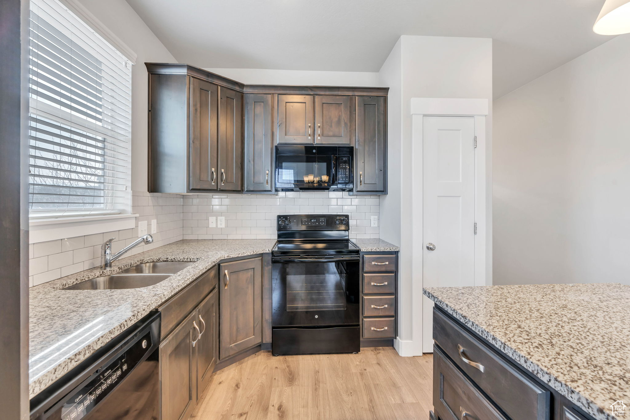 Kitchen with decorative backsplash, sink, light stone countertops, and black appliances