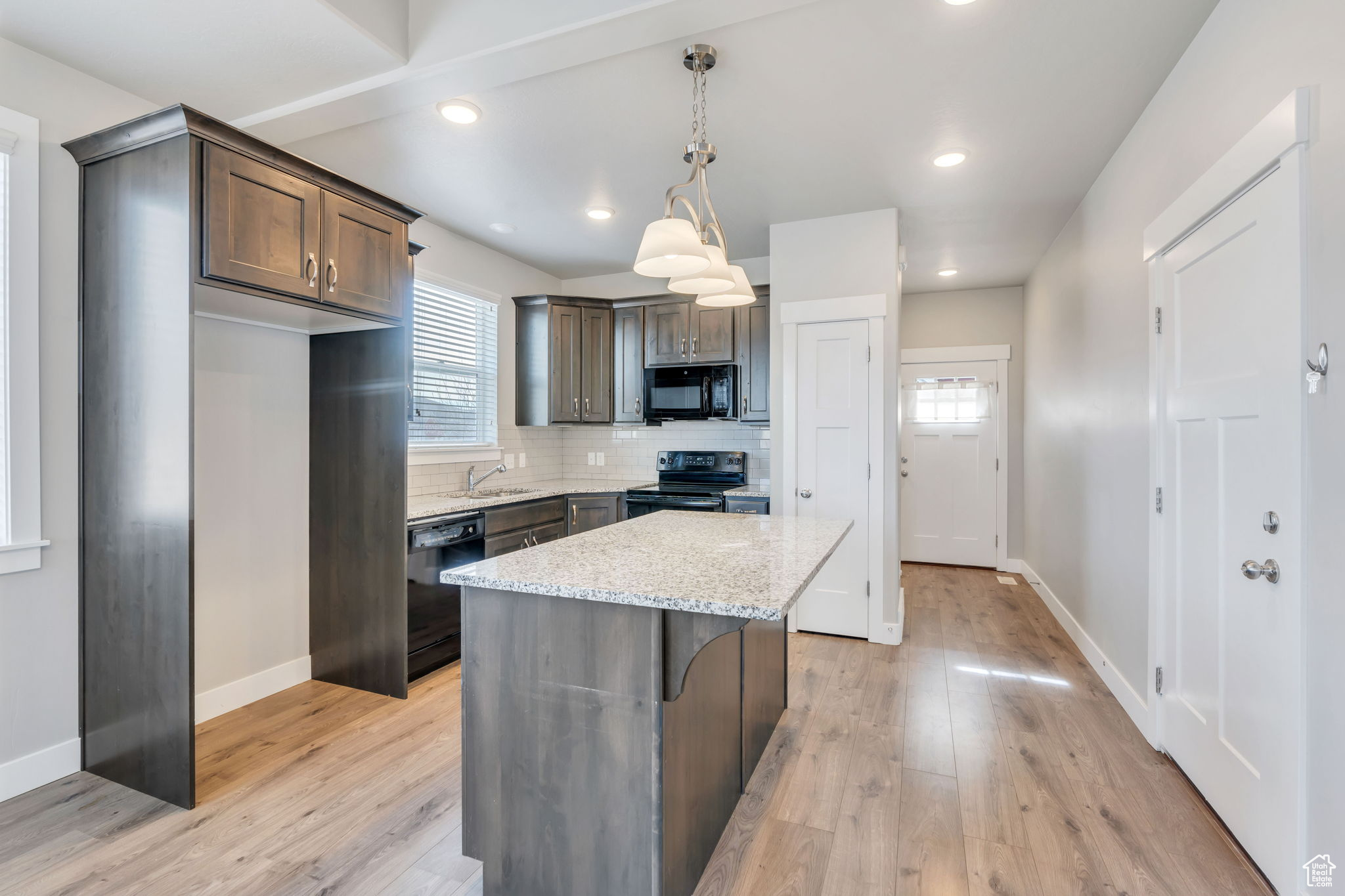 Kitchen with hanging light fixtures, light stone counters, decorative backsplash, a kitchen island, and black appliances