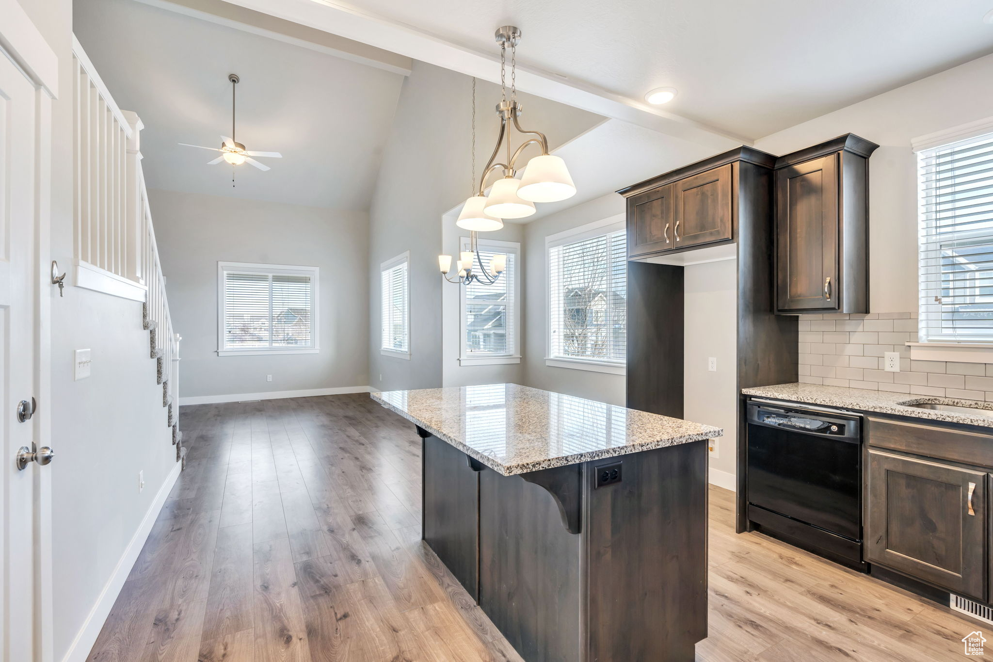 Kitchen with a kitchen breakfast bar, decorative backsplash, black dishwasher, dark brown cabinets, and light stone counters