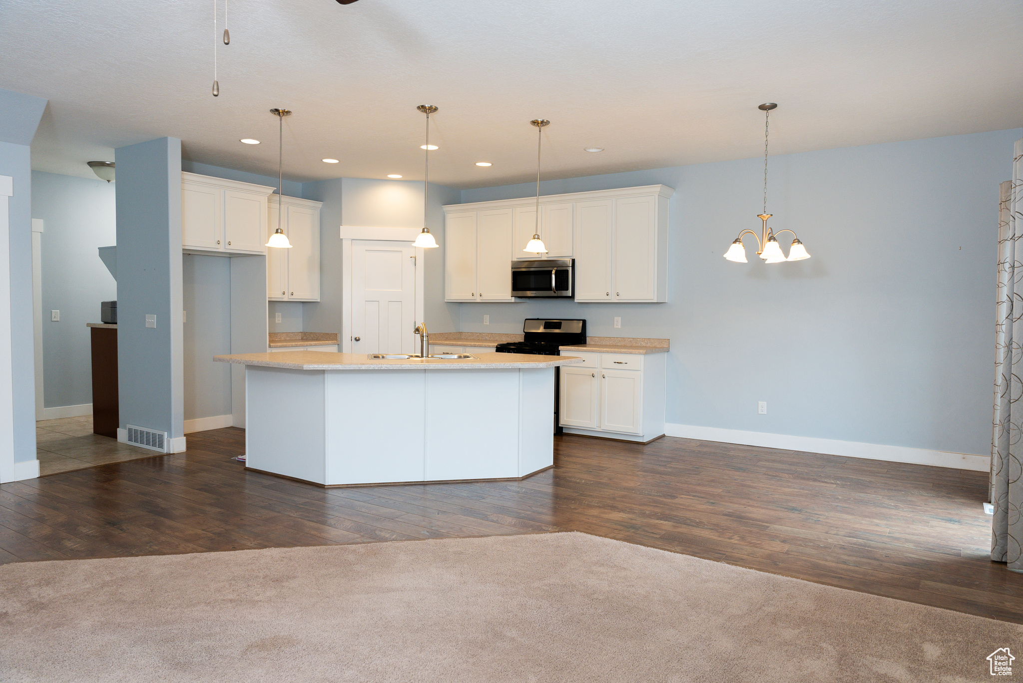 Kitchen with a center island with sink, white cabinets, hanging light fixtures, and appliances with stainless steel finishes