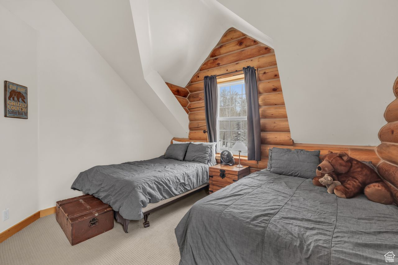 Carpeted bedroom with log walls and lofted ceiling