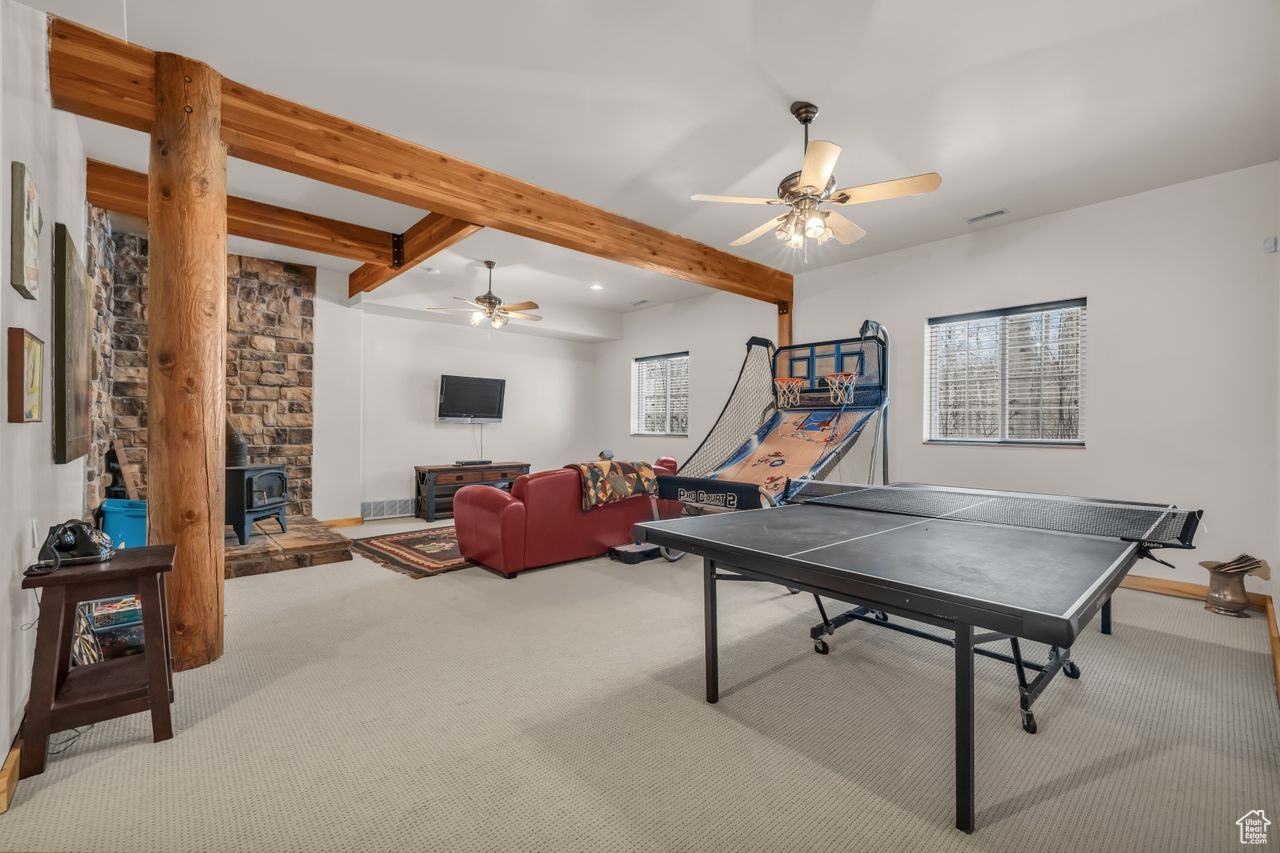 Recreation room with beamed ceiling, carpet flooring, a wood stove, and ceiling fan