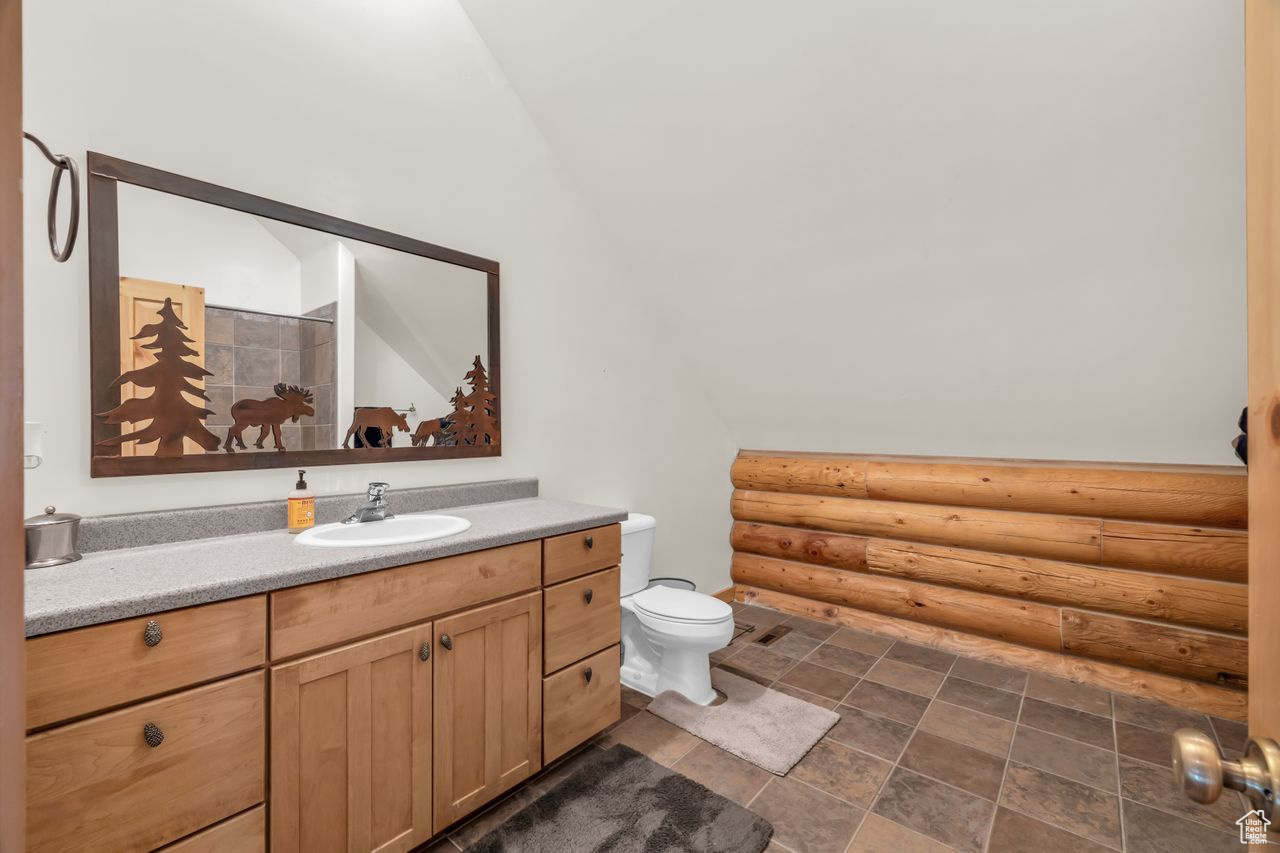 Bathroom featuring vanity, log walls, vaulted ceiling, and toilet