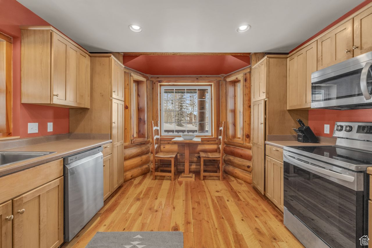 Kitchen with sink, light brown cabinets, log walls, stainless steel appliances, and light hardwood / wood-style floors