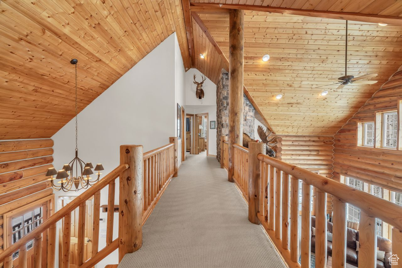 Hallway with rustic walls, a chandelier, wood ceiling, and vaulted ceiling