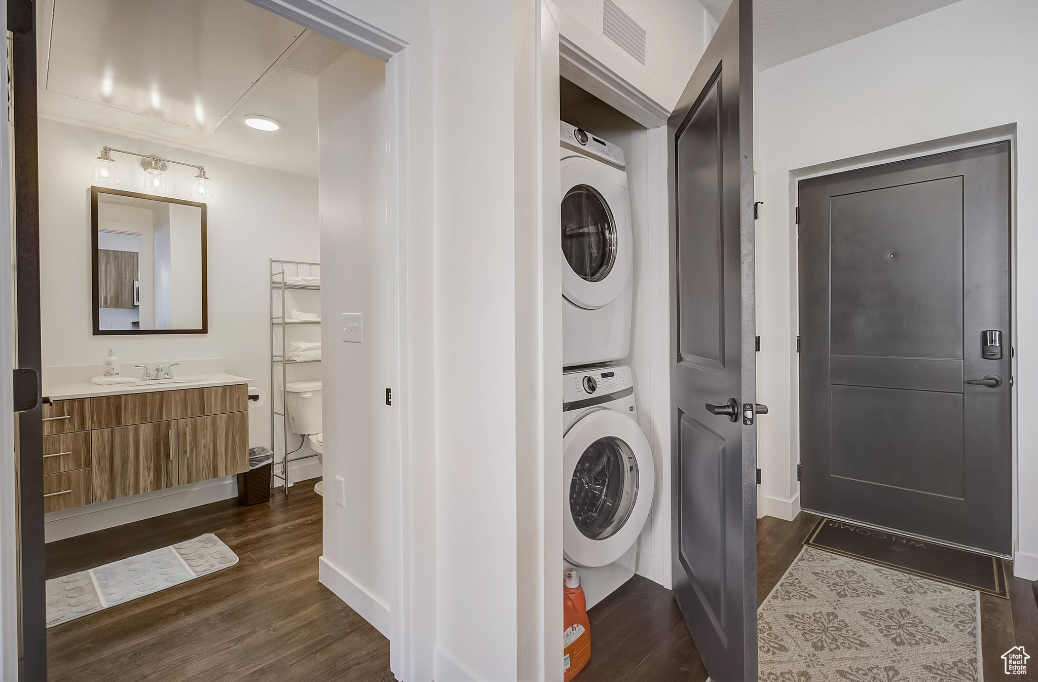Laundry area featuring dark hardwood / wood-style floors, stacked washer / drying machine, and sink