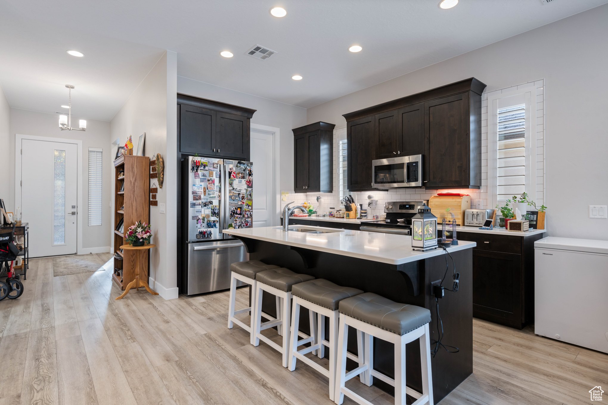 Kitchen with decorative backsplash, appliances with stainless steel finishes, light wood-type flooring, sink, and a center island with sink