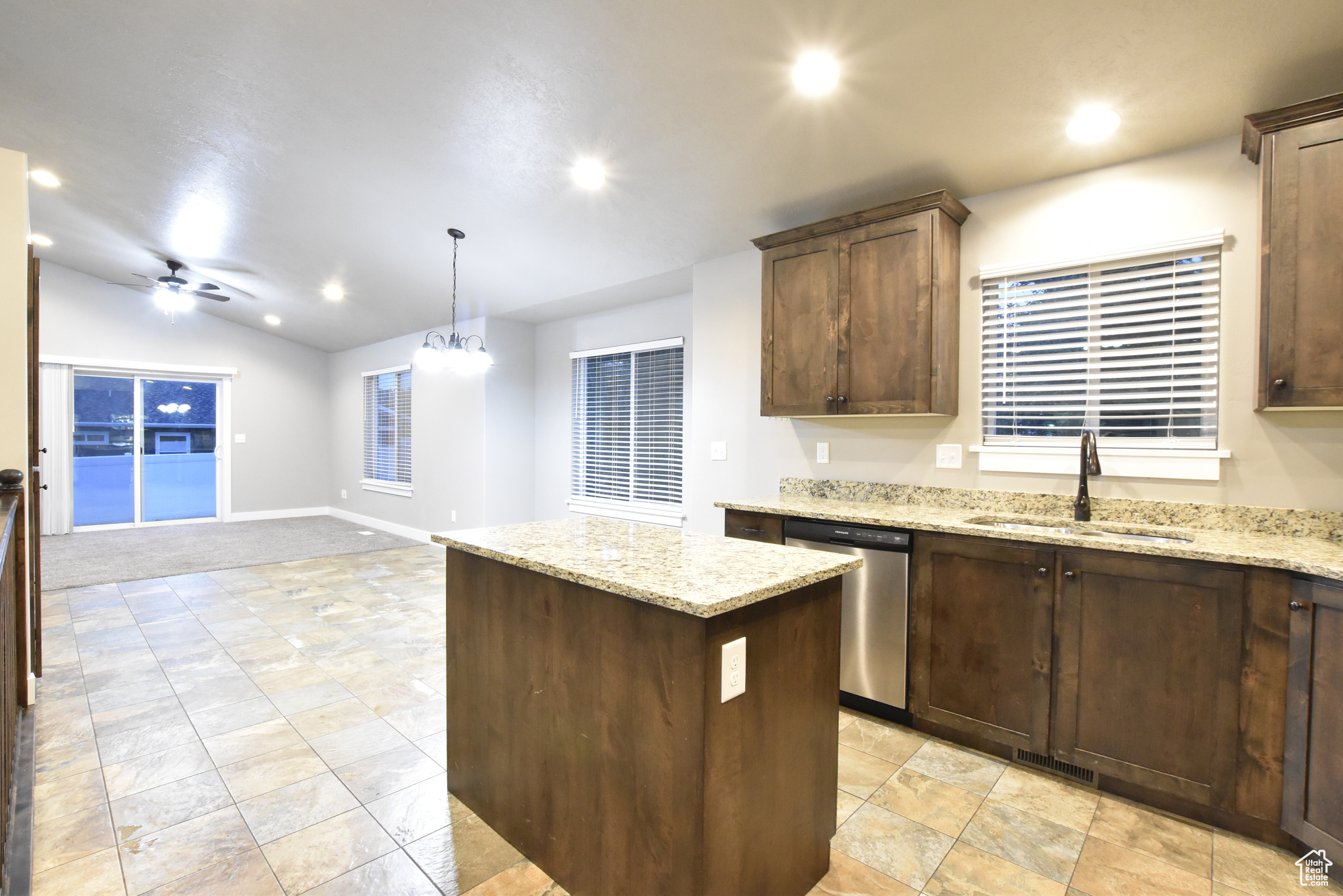 Kitchen with a center island, ceiling fan with notable chandelier, sink, stainless steel dishwasher, and light stone counters