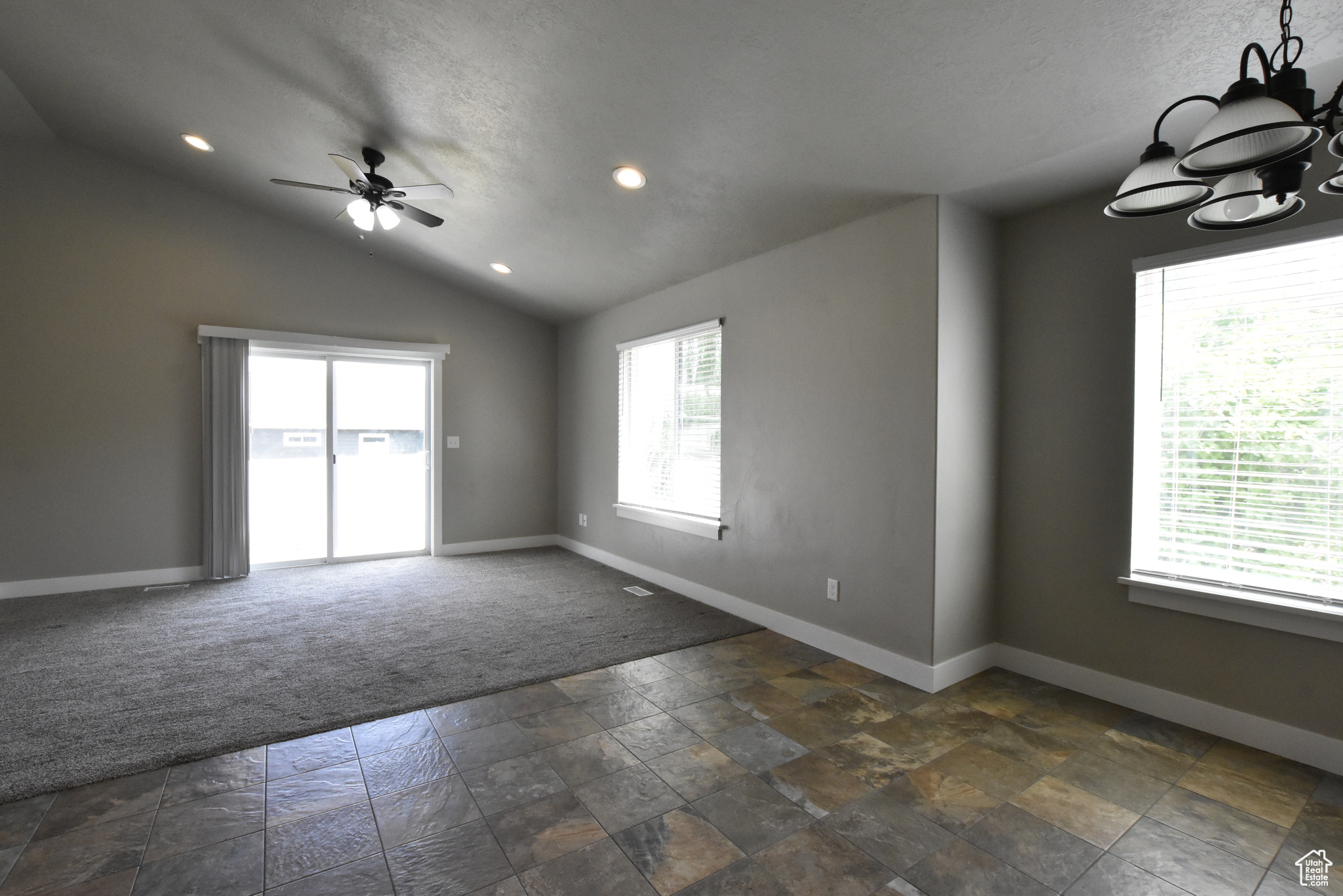 Empty room with ceiling fan, dark carpet, and vaulted ceiling